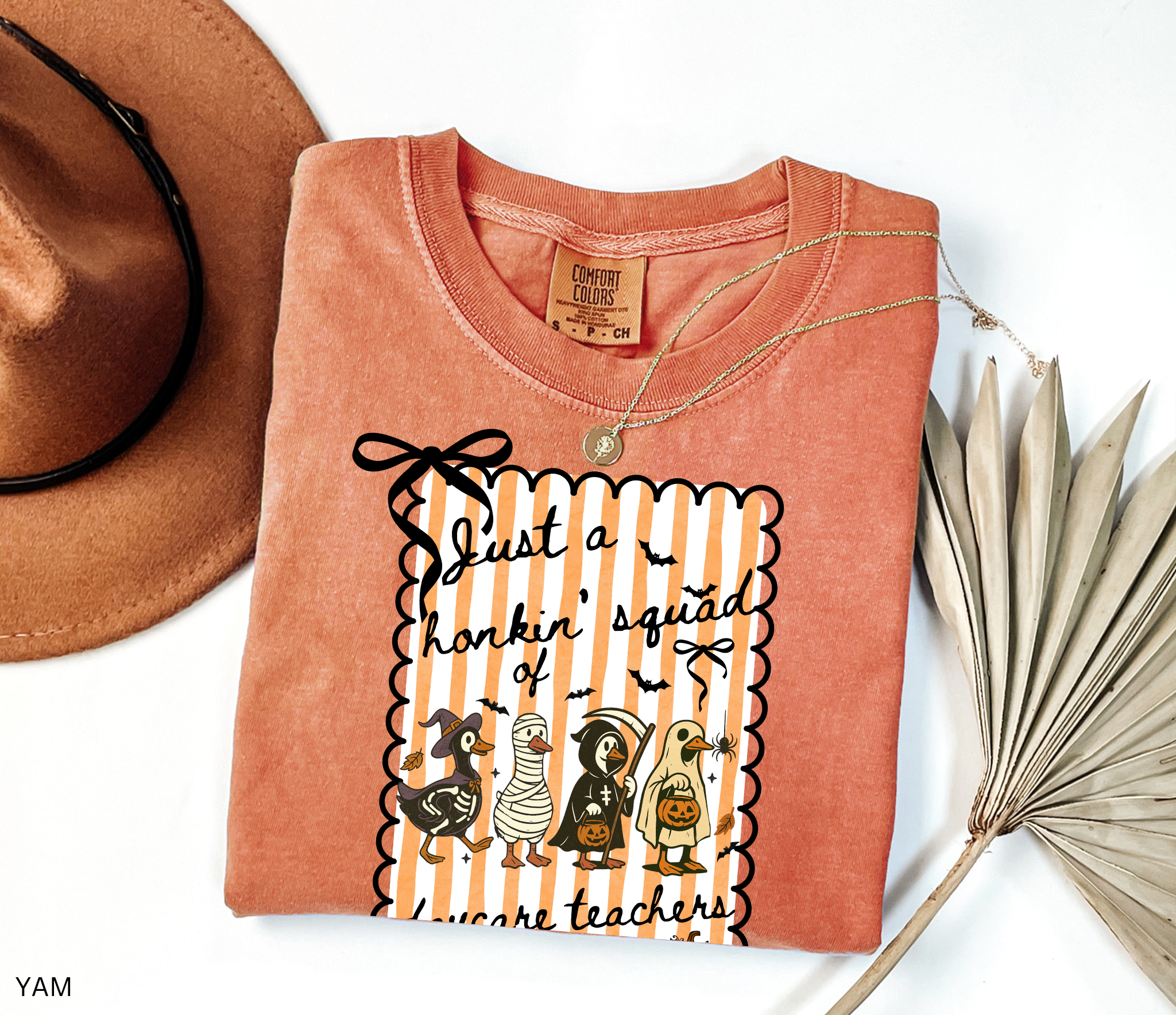 Halloween daycare teacher shirt featuring four geese dressed in spooky costumes (witch, mummy, reaper, ghost) with pumpkins, bats, and candy on orange striped background. Perfect group Halloween tee for daycare teachers.