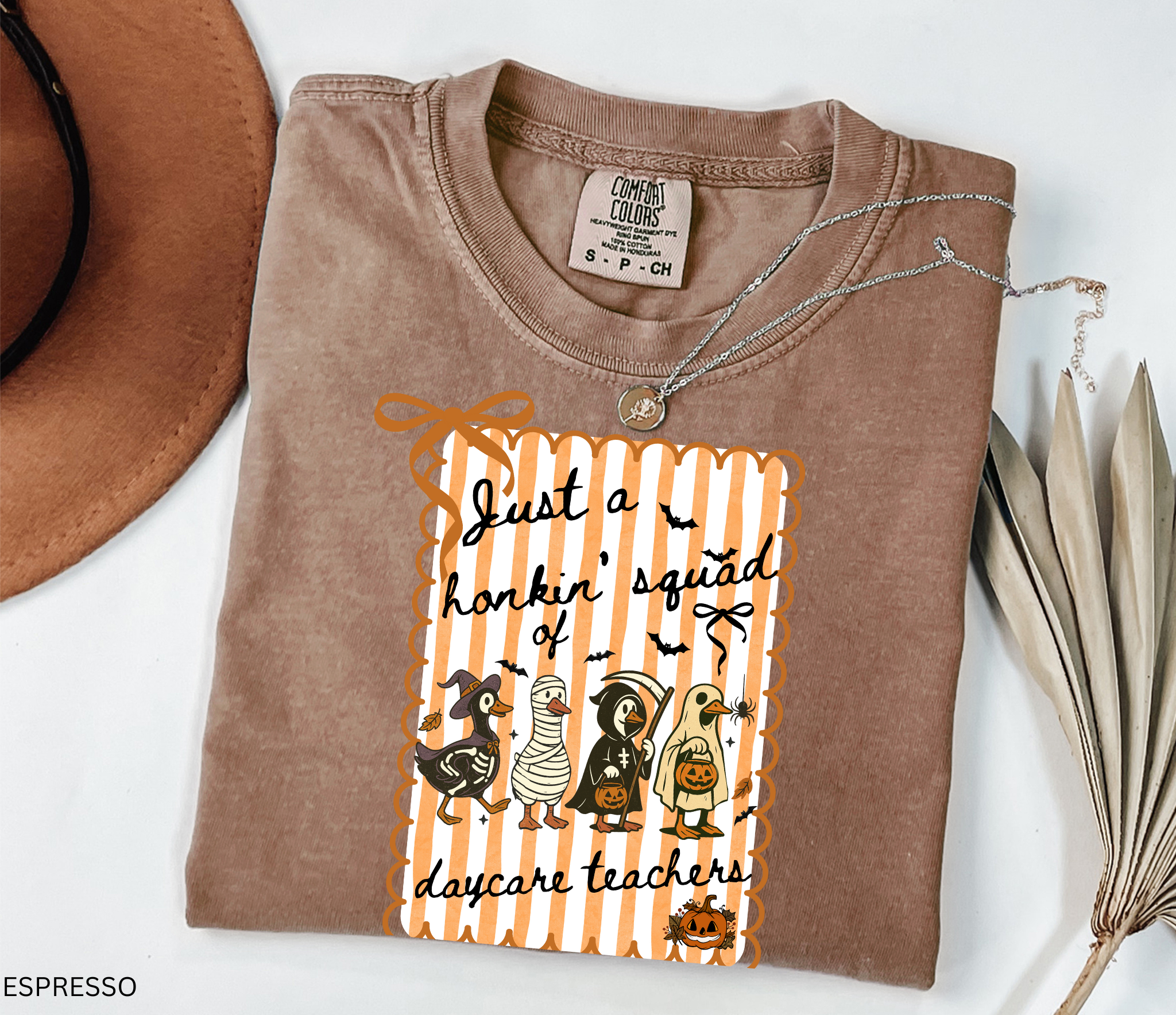 Halloween daycare teacher shirt featuring four geese dressed in spooky costumes (witch, mummy, reaper, ghost) with pumpkins, bats, and candy on orange striped background. Perfect group Halloween tee for daycare teachers.