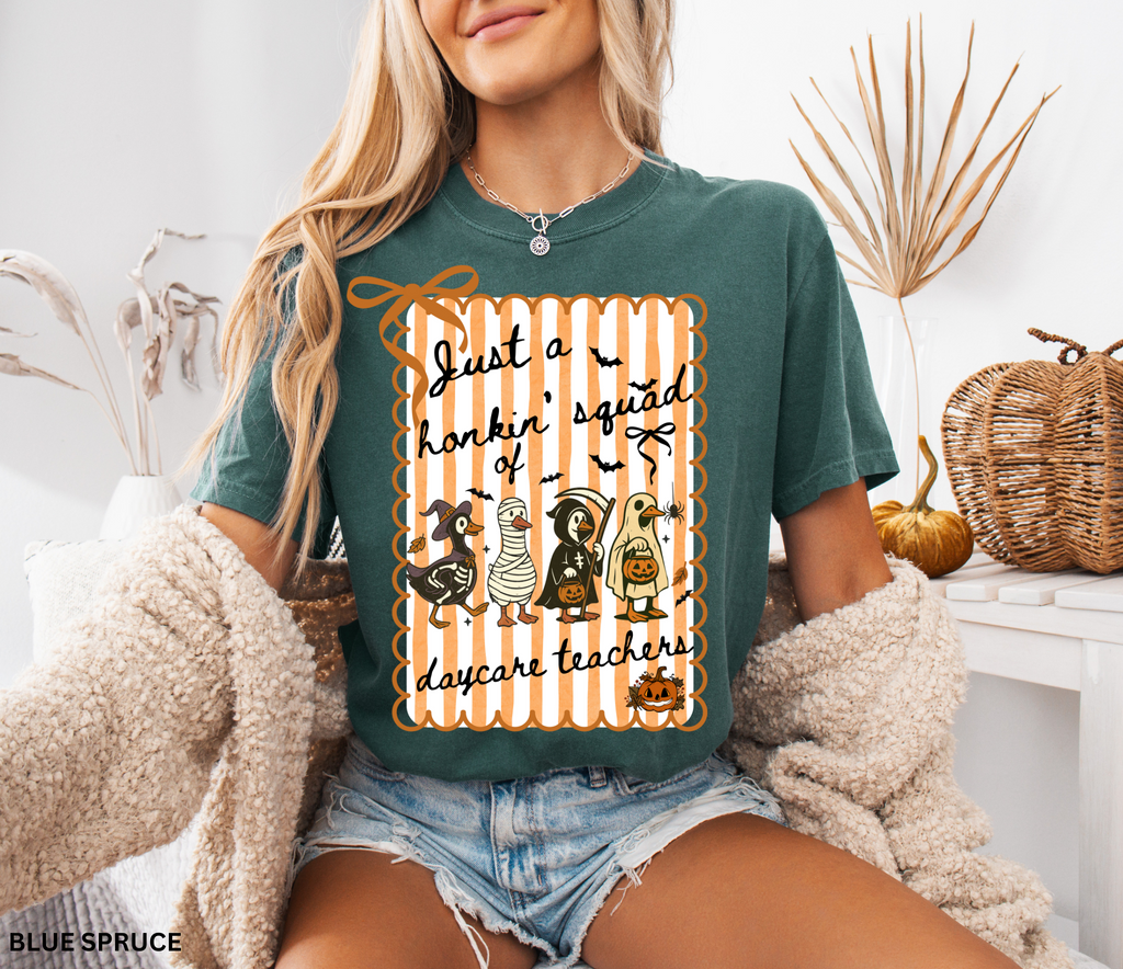 Halloween daycare teacher shirt featuring four geese dressed in spooky costumes (witch, mummy, reaper, ghost) with pumpkins, bats, and candy on orange striped background. Perfect group Halloween tee for daycare teachers.