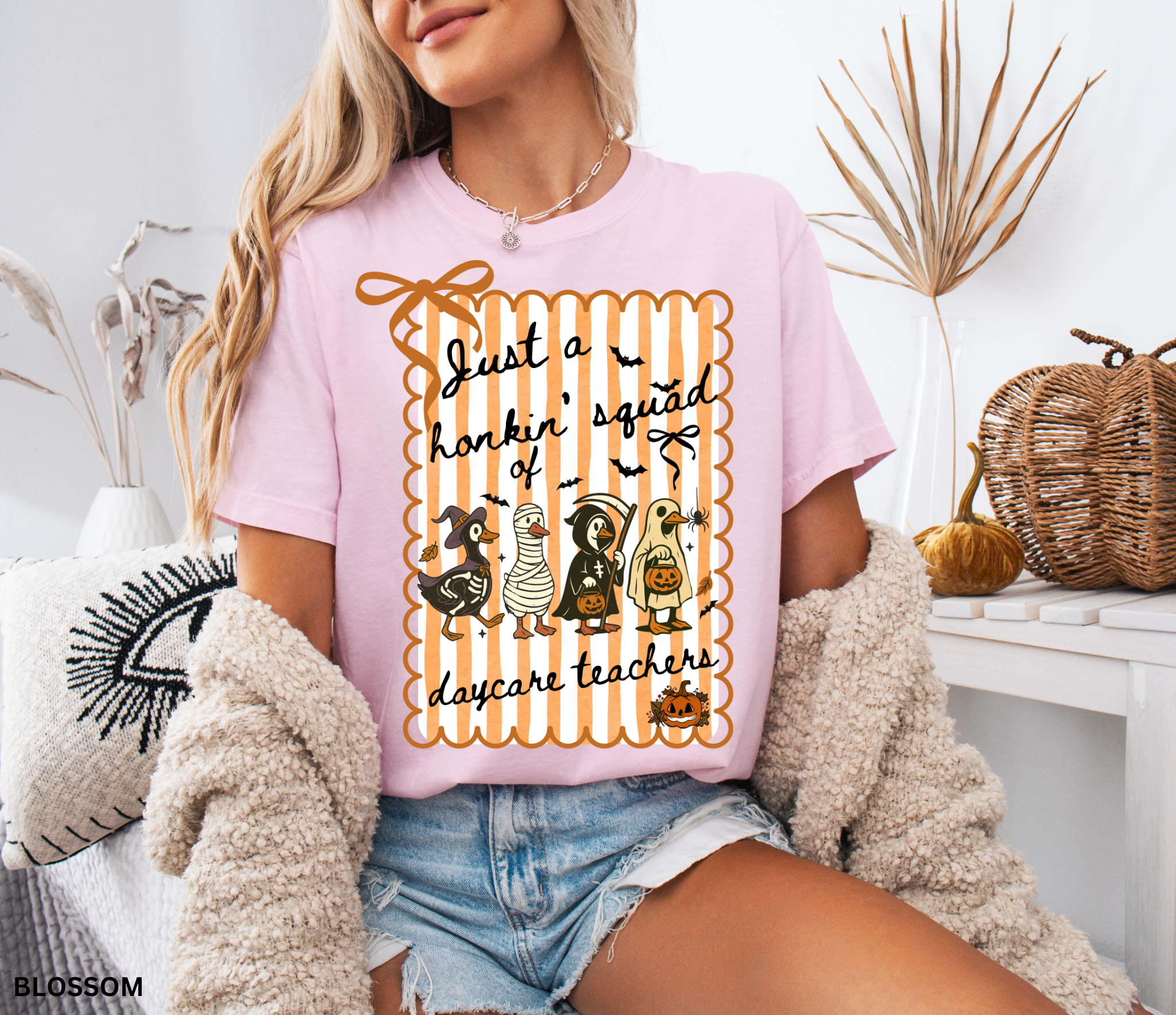 Halloween daycare teacher shirt featuring four geese dressed in spooky costumes (witch, mummy, reaper, ghost) with pumpkins, bats, and candy on orange striped background. Perfect group Halloween tee for daycare teachers.
