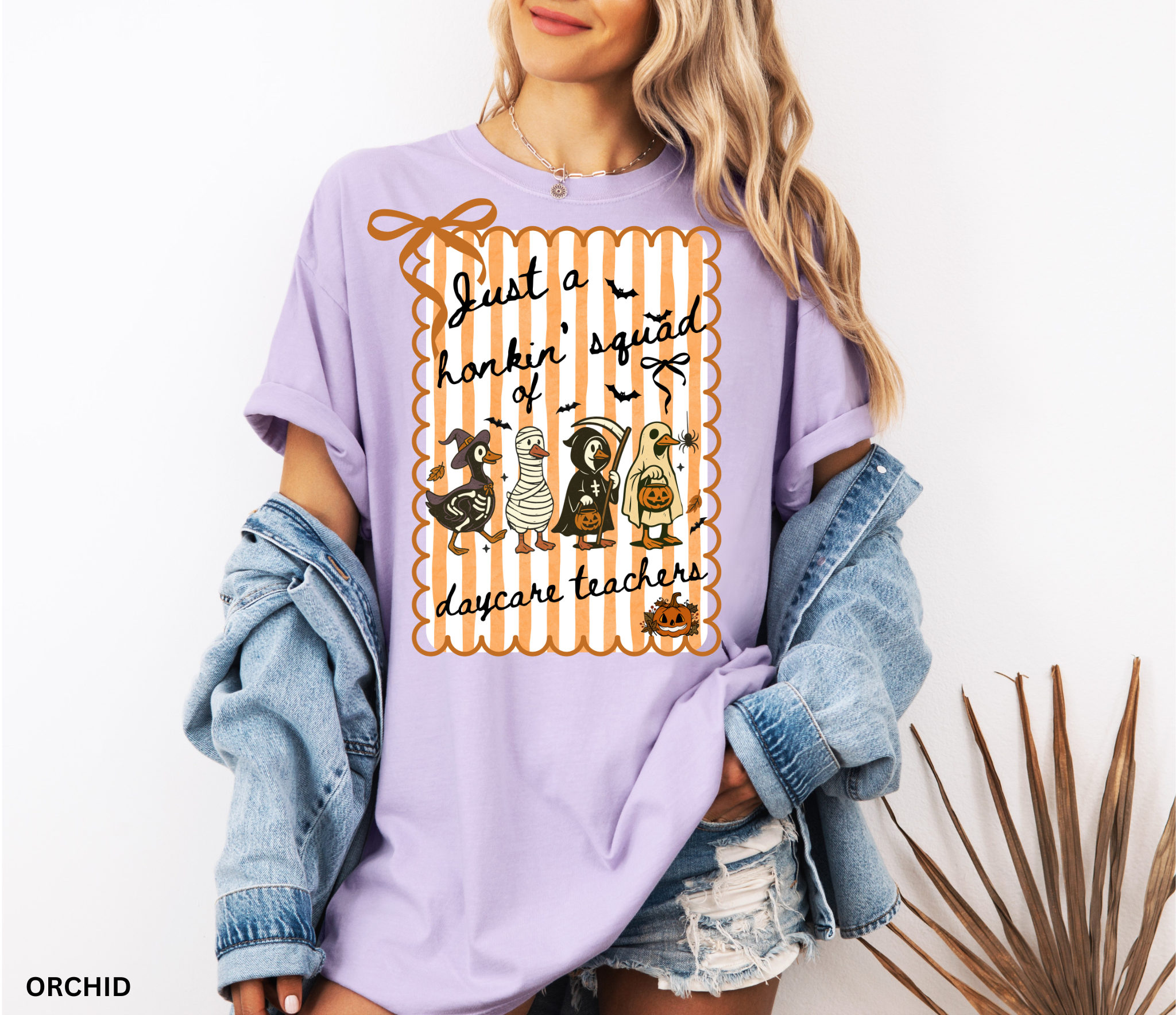 Halloween daycare teacher shirt featuring four geese dressed in spooky costumes (witch, mummy, reaper, ghost) with pumpkins, bats, and candy on orange striped background. Perfect group Halloween tee for daycare teachers.