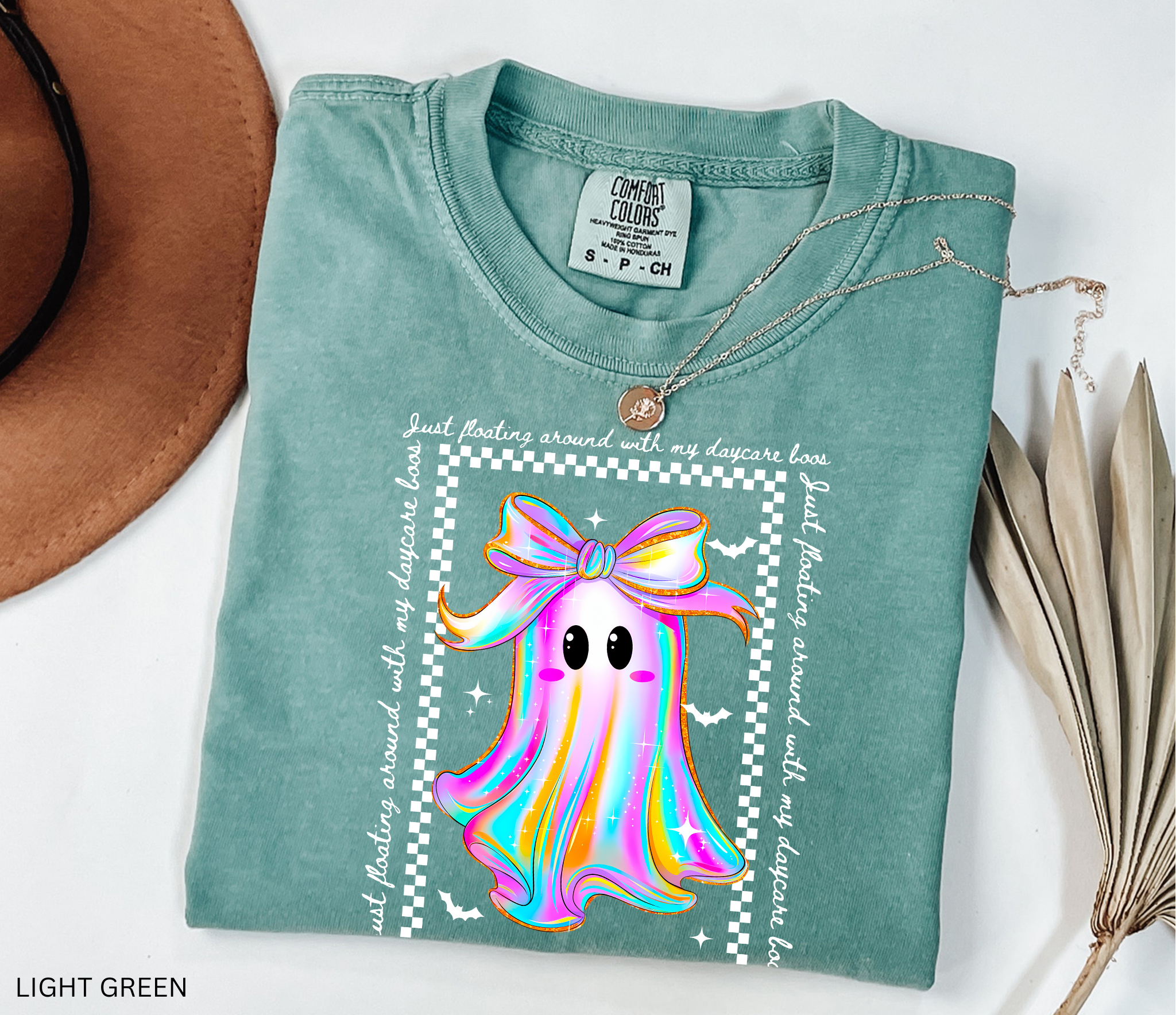 Daycare teacher Halloween shirt with rainbow ghost wearing a big bow, surrounded by stars and bats, with the phrase “Just Floating Around With My Daycare Boos.” Cute spooky season tee for childcare workers.