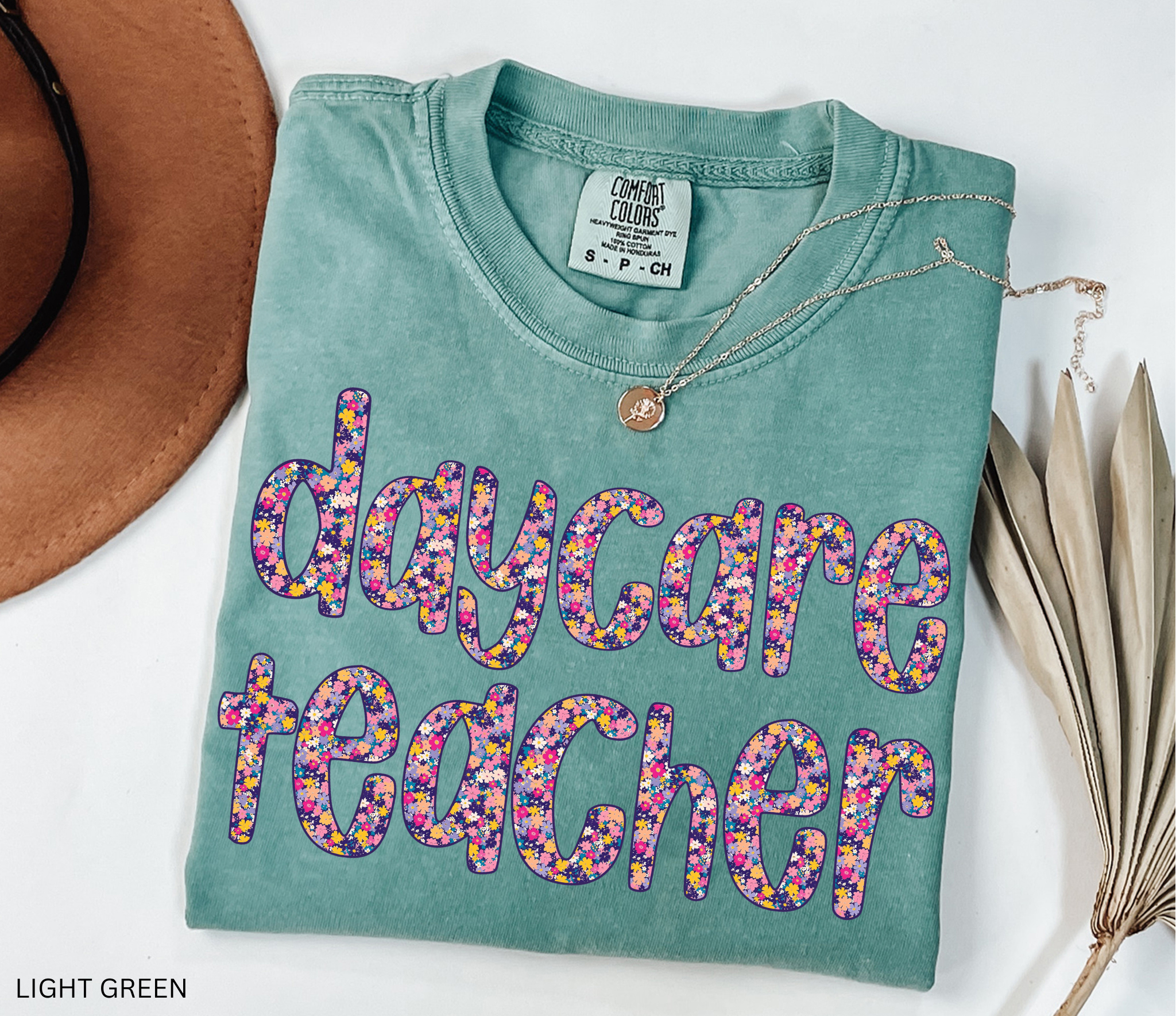 Daycare teacher shirt with bold floral text design in bright colors, fun and cheerful tee for childcare workers and preschool teachers.
