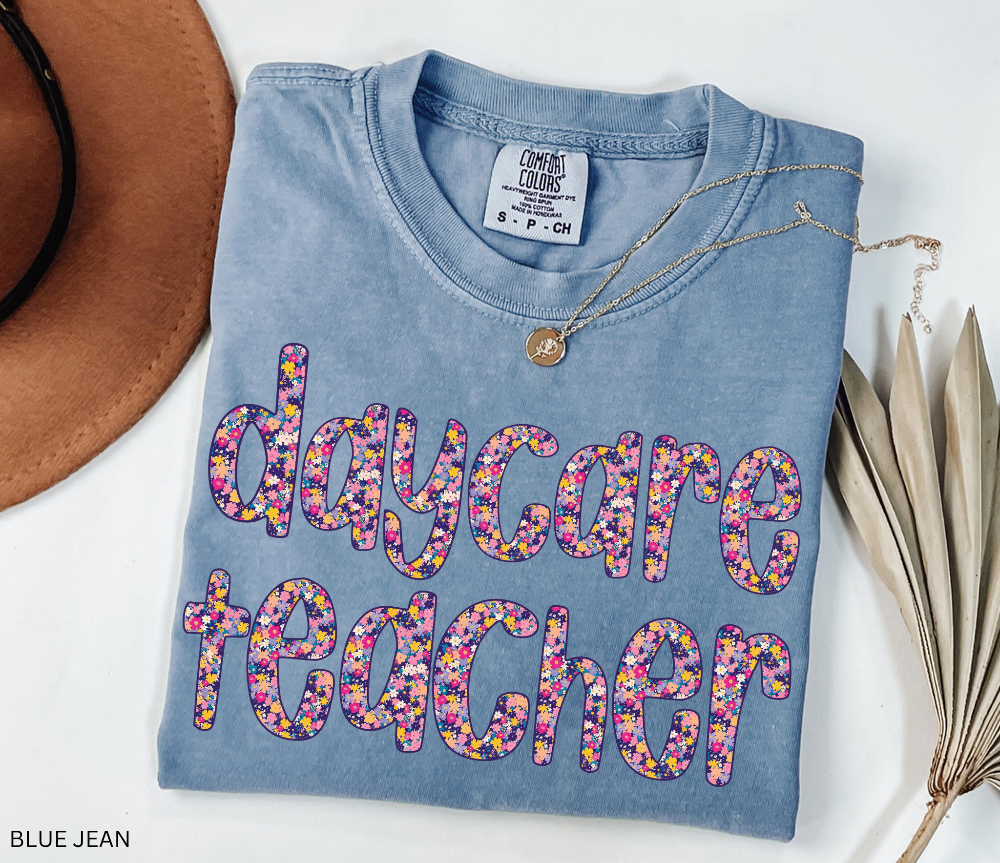 Daycare teacher shirt with bold floral text design in bright colors, fun and cheerful tee for childcare workers and preschool teachers.