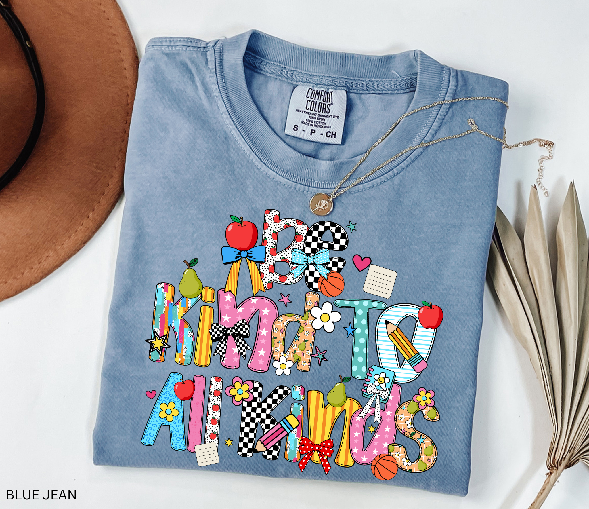 Colorful “Be Kind to All Kinds” teacher shirt with playful letters, apples, pears, bows, flowers, and school-themed accents.