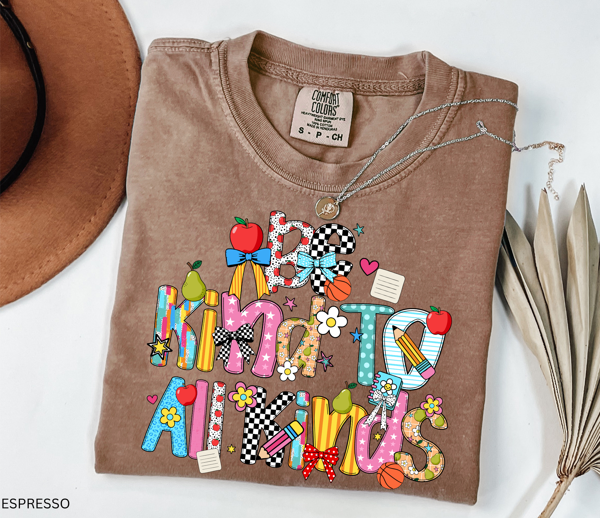 Colorful “Be Kind to All Kinds” teacher shirt with playful letters, apples, pears, bows, flowers, and school-themed accents.
