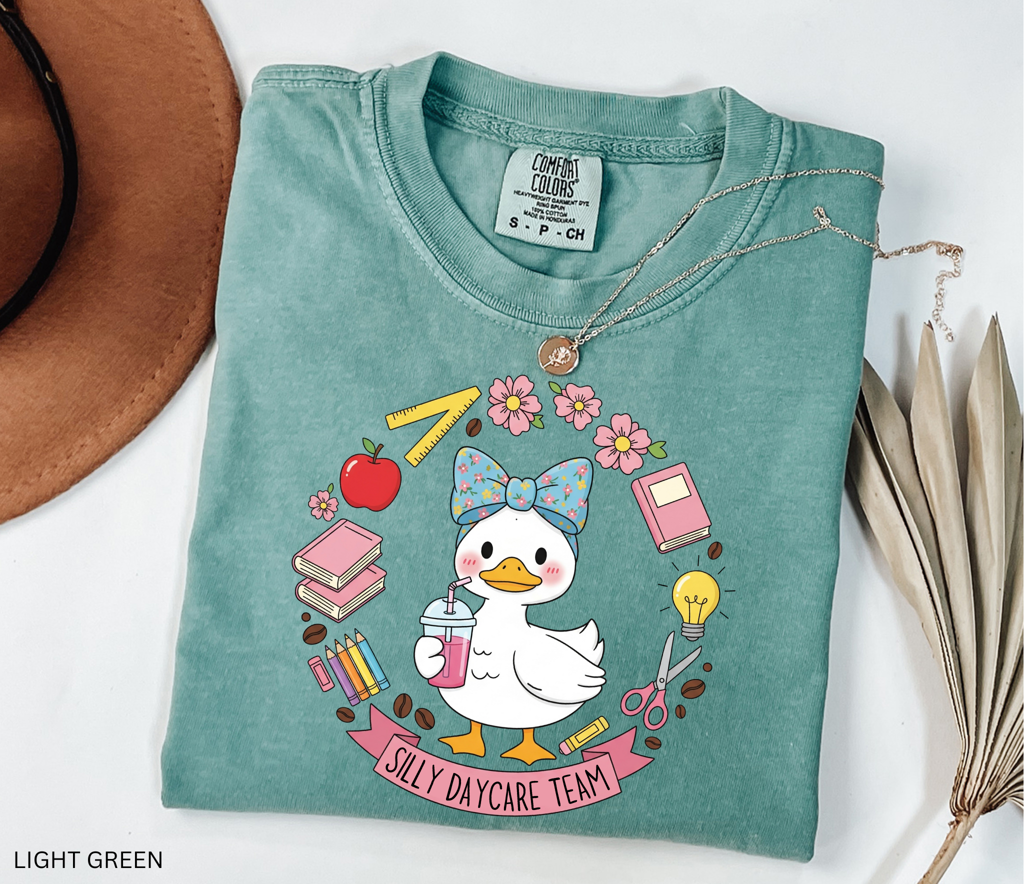 Cute goose in a floral bow holding a drink, surrounded by books, pencils, apple, ruler, flowers, scissors, and lightbulb with banner reading “Silly Daycare Team.”