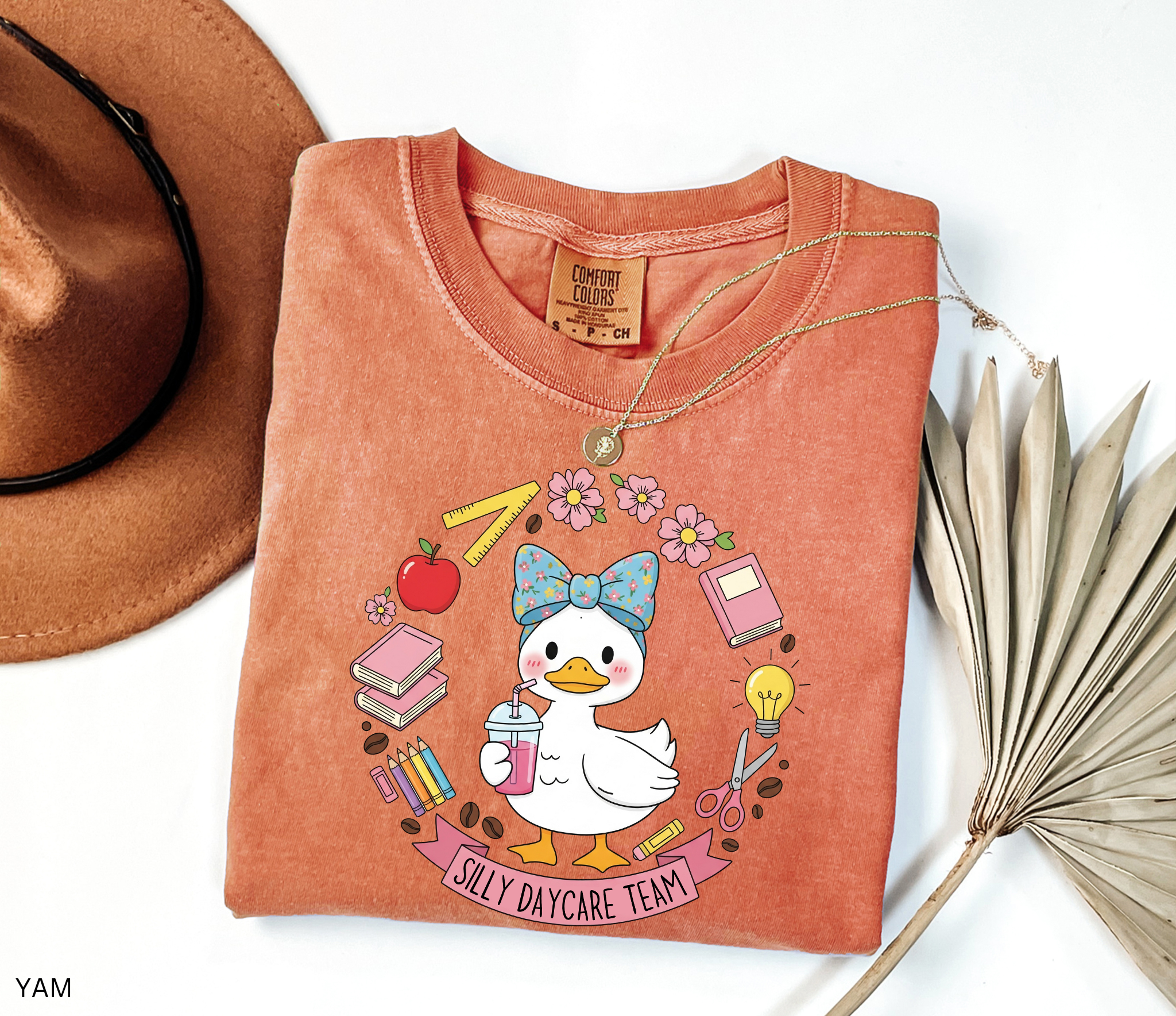 Cute goose in a floral bow holding a drink, surrounded by books, pencils, apple, ruler, flowers, scissors, and lightbulb with banner reading “Silly Daycare Team.”