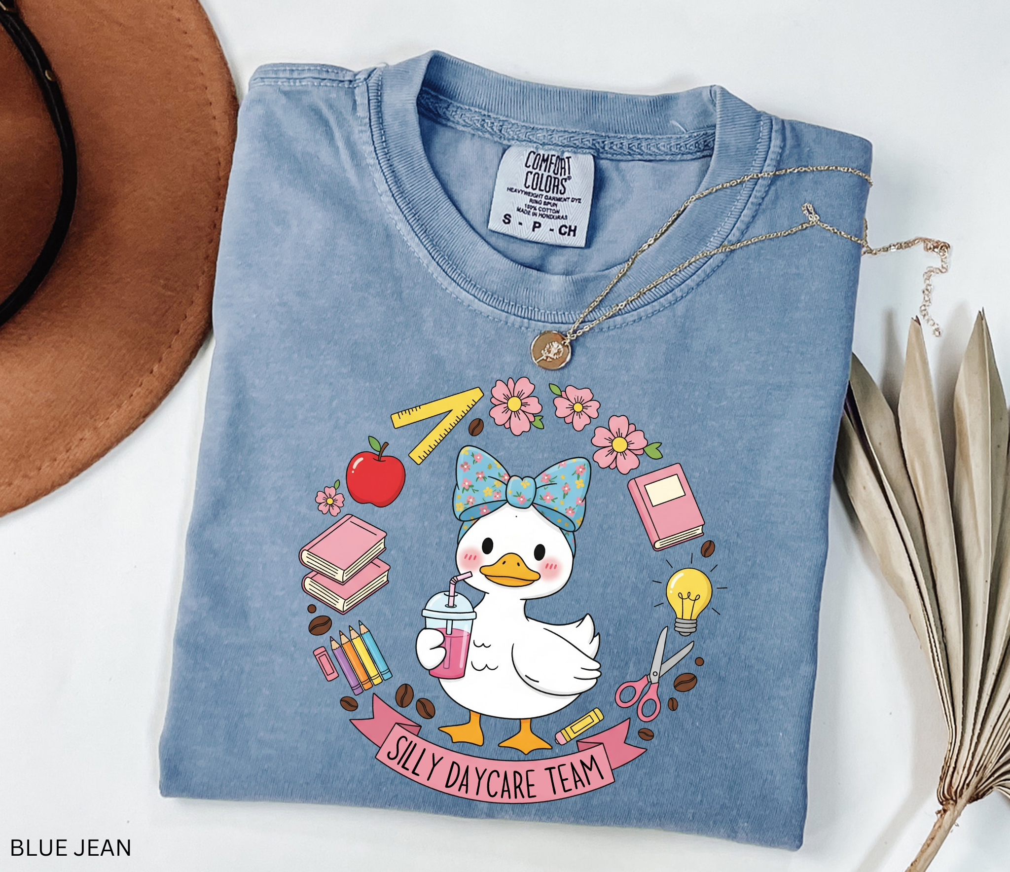Cute goose in a floral bow holding a drink, surrounded by books, pencils, apple, ruler, flowers, scissors, and lightbulb with banner reading “Silly Daycare Team.”