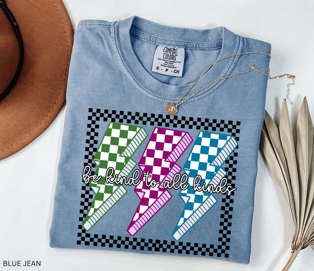 Checkerboard lightning bolt “Be Kind to All Kinds” shirt in retro green, pink, and blue design – inclusive teacher graphic tee.