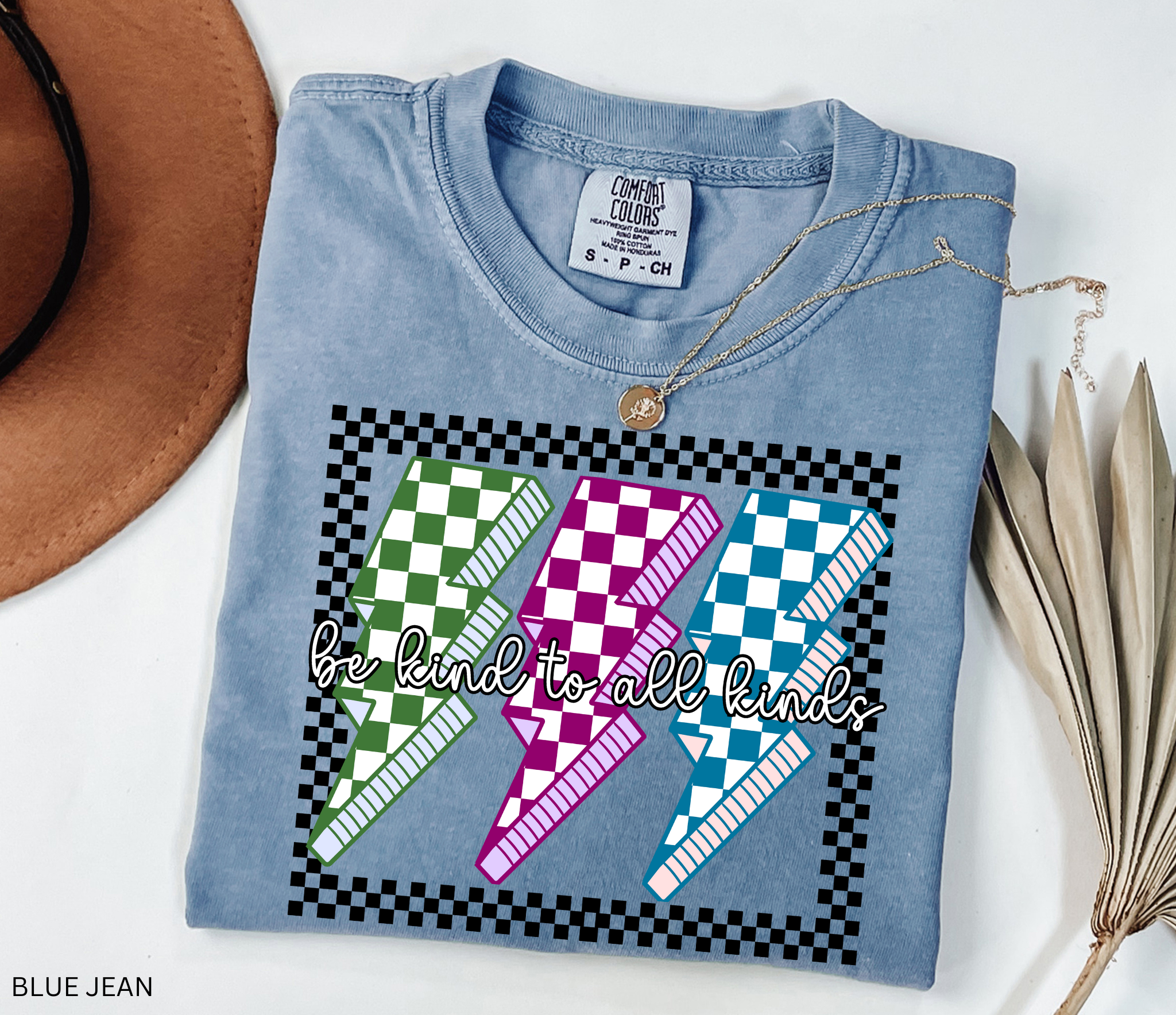 Checkerboard lightning bolt “Be Kind to All Kinds” shirt in retro green, pink, and blue design – inclusive teacher graphic tee.