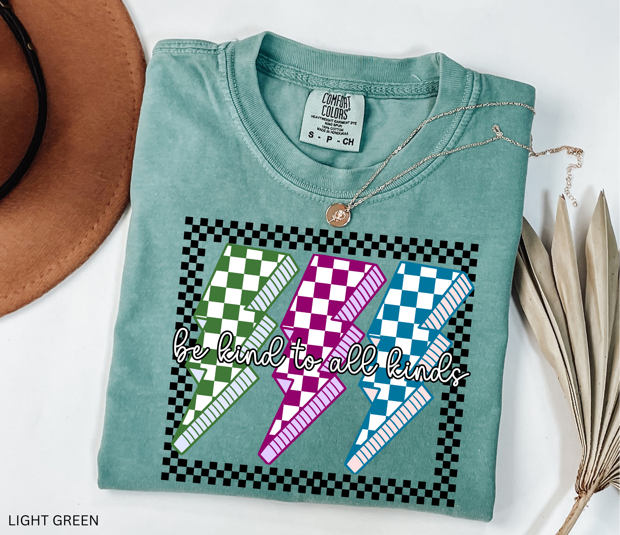 Checkerboard lightning bolt “Be Kind to All Kinds” shirt in retro green, pink, and blue design – inclusive teacher graphic tee.