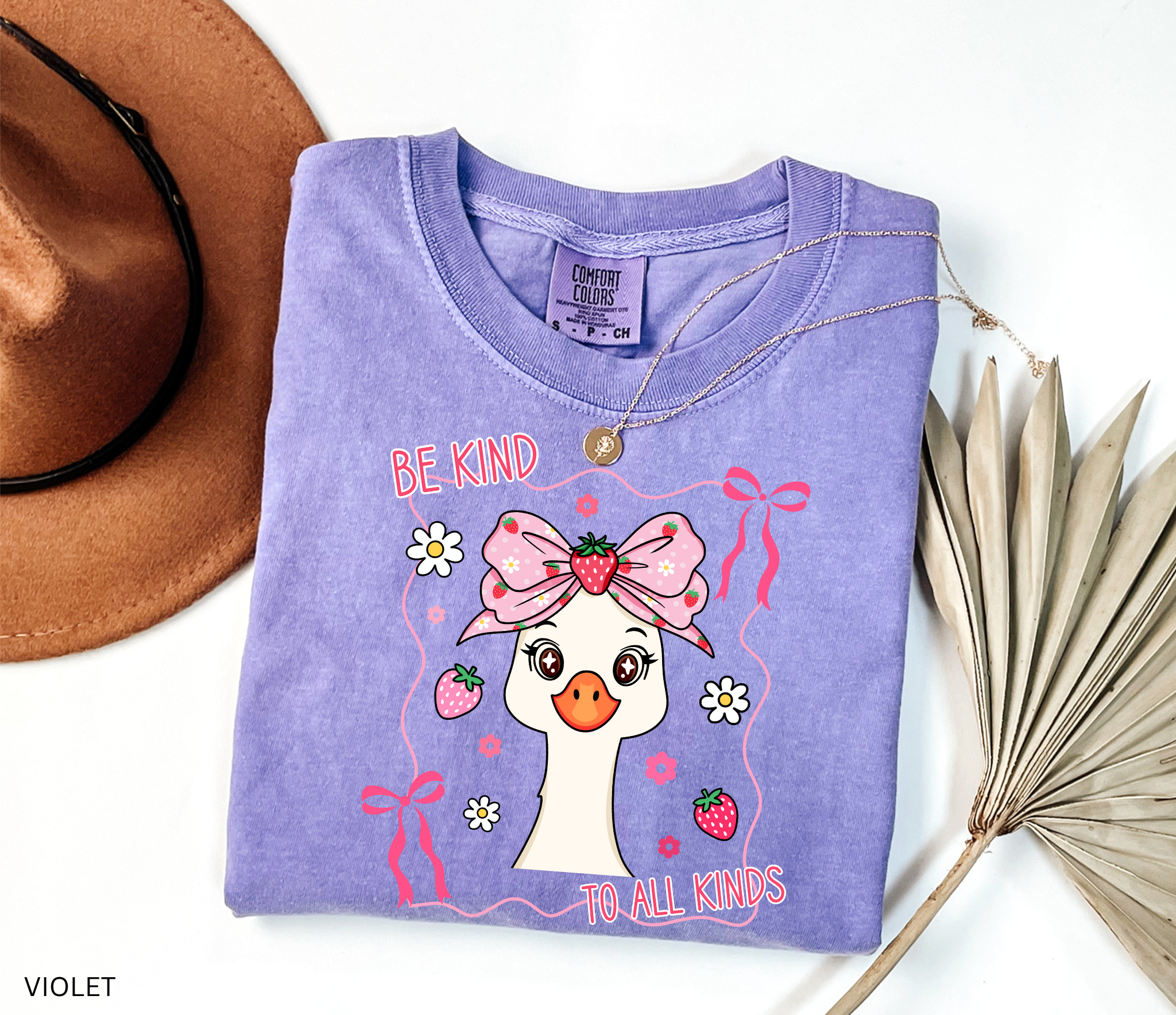 Goose with strawberry bow and flowers framed in ribbons with the phrase “Be Kind to All Kinds.”