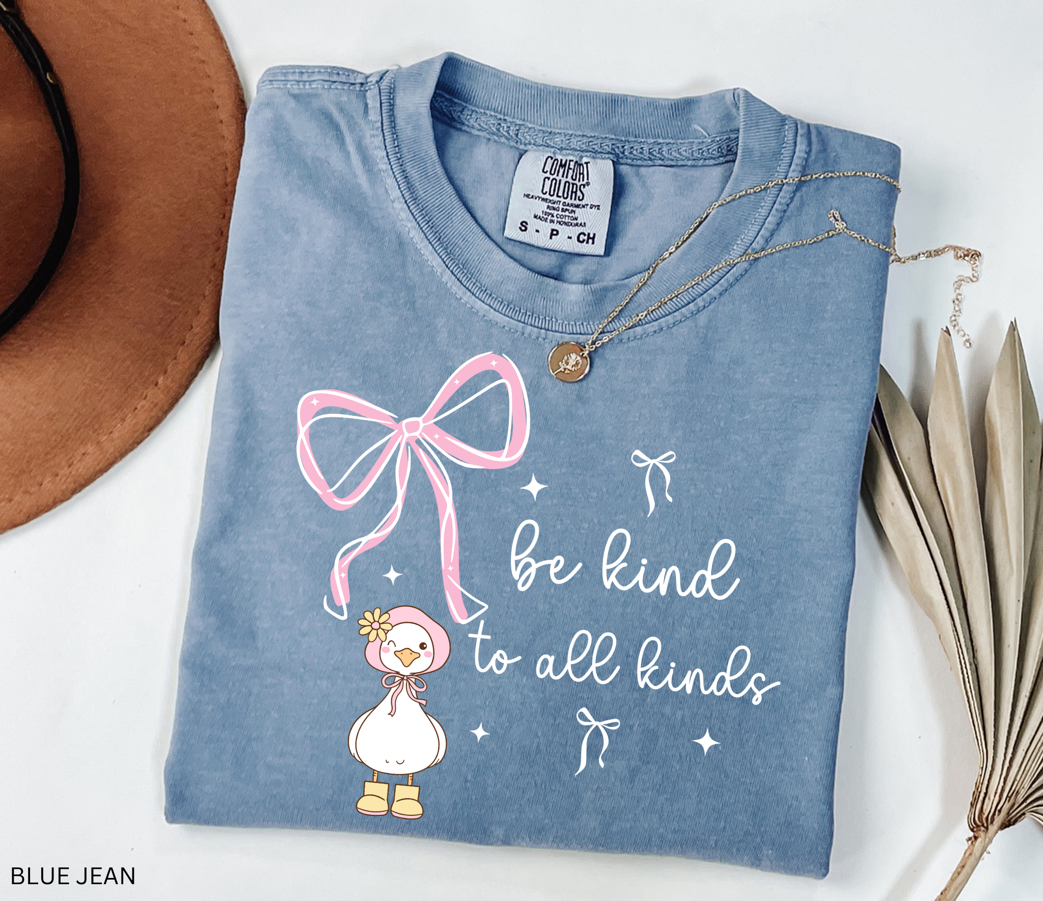 Cute goose wearing a pink bonnet with flower and boots, large pink bow above, and the words “Be Kind to All Kinds.”