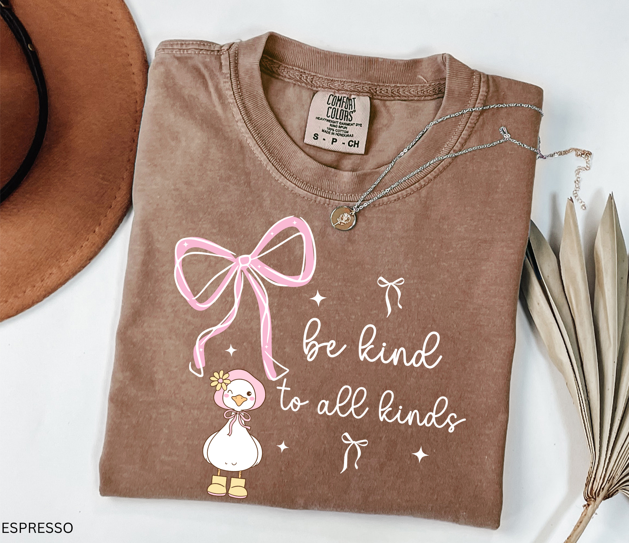 Cute goose wearing a pink bonnet with flower and boots, large pink bow above, and the words “Be Kind to All Kinds.”