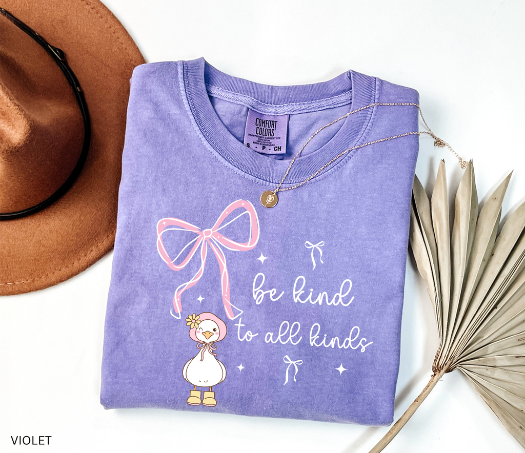 Cute goose wearing a pink bonnet with flower and boots, large pink bow above, and the words “Be Kind to All Kinds.”
