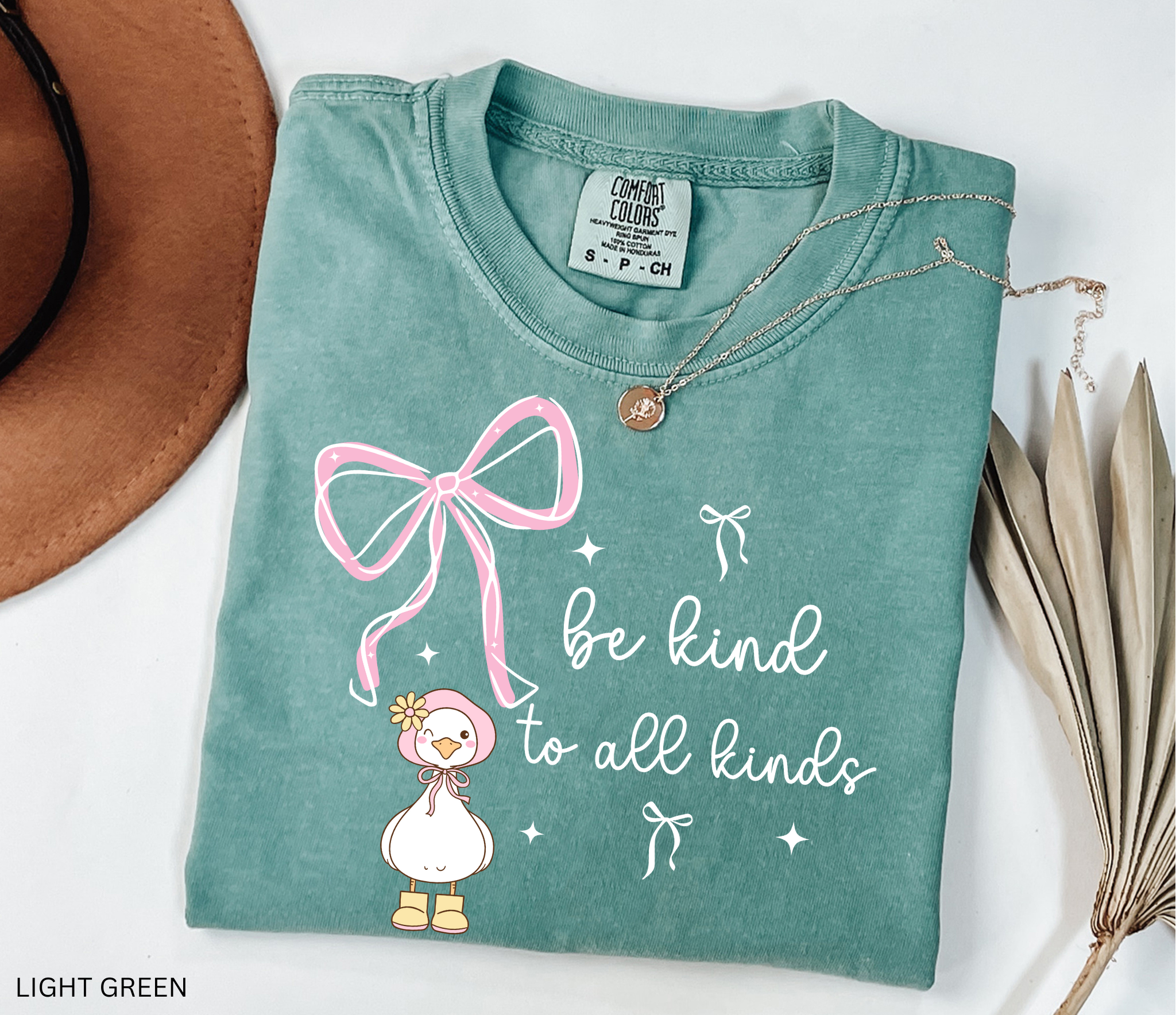 Cute goose wearing a pink bonnet with flower and boots, large pink bow above, and the words “Be Kind to All Kinds.”