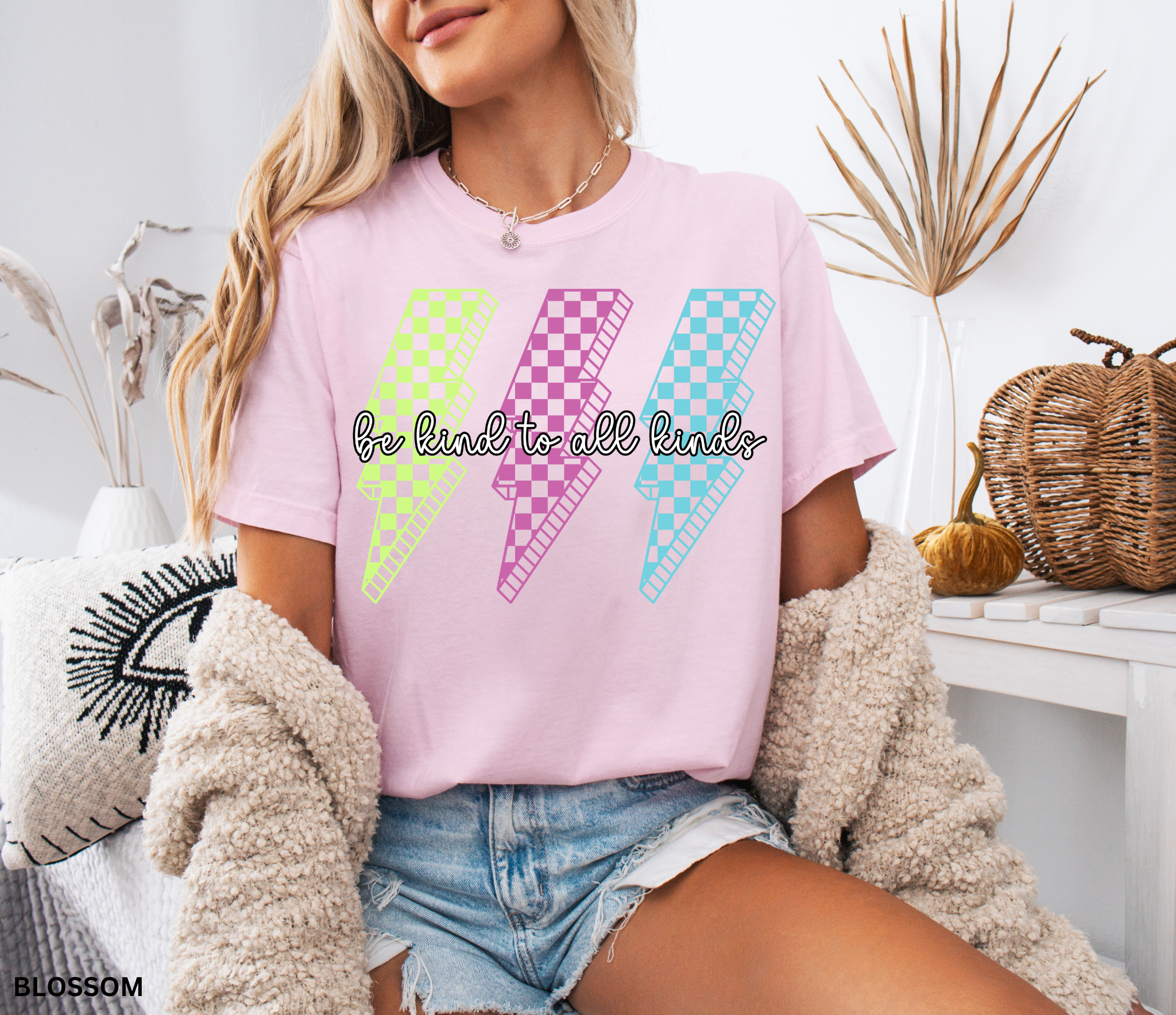 Three retro lightning bolts in neon green, pink, and blue checkered patterns with the phrase “Be Kind to All Kinds.”