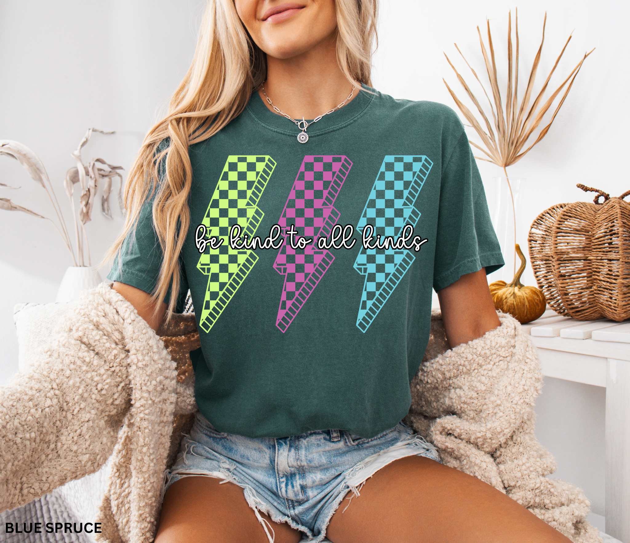 Three retro lightning bolts in neon green, pink, and blue checkered patterns with the phrase “Be Kind to All Kinds.”