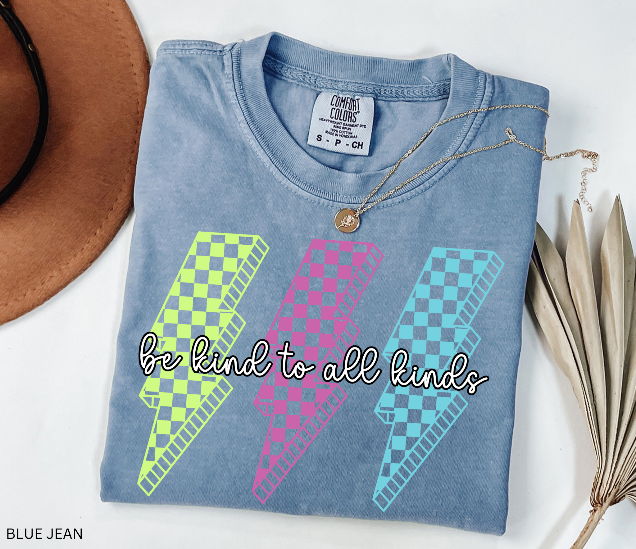 Three retro lightning bolts in neon green, pink, and blue checkered patterns with the phrase “Be Kind to All Kinds.”