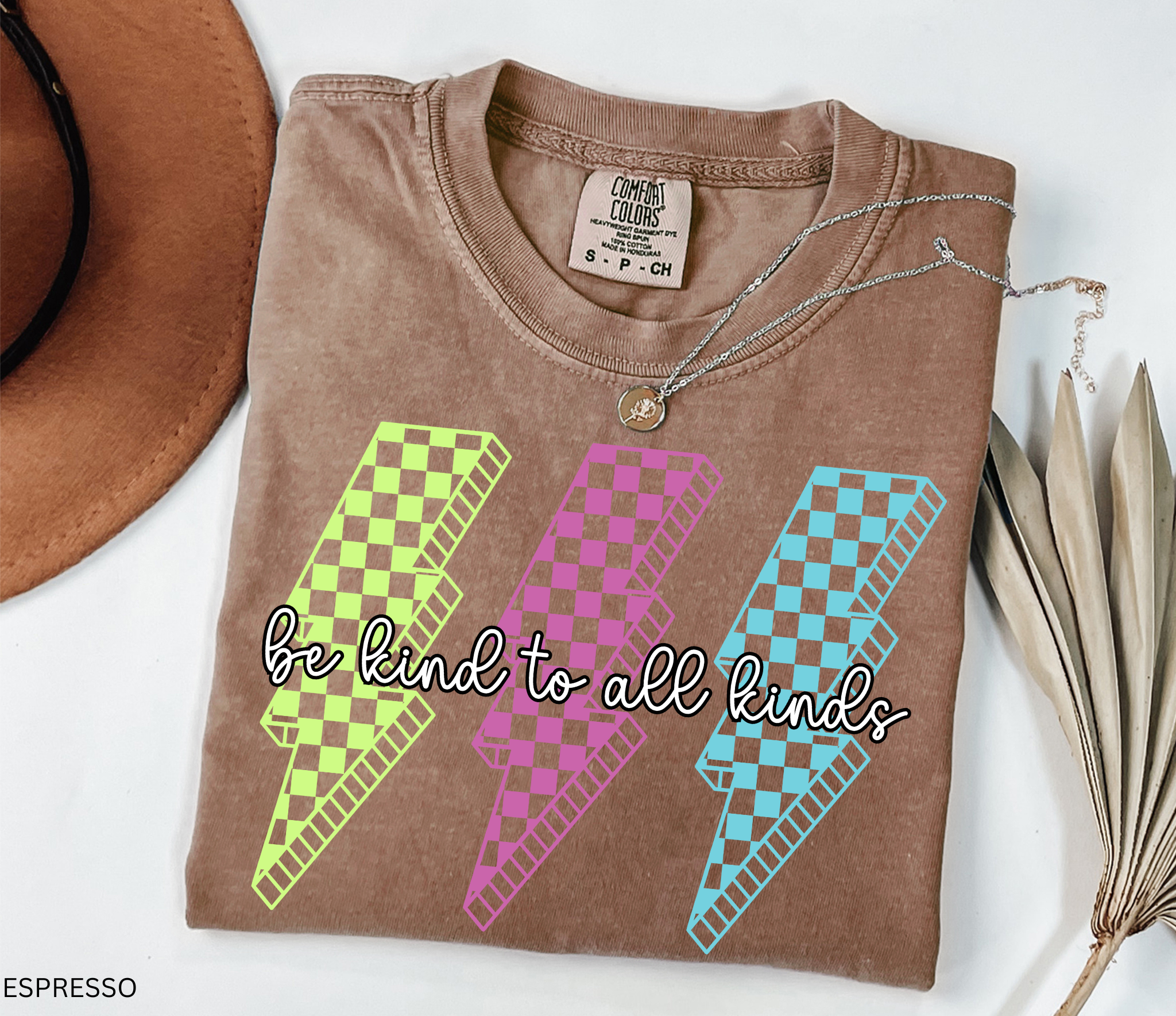 Three retro lightning bolts in neon green, pink, and blue checkered patterns with the phrase “Be Kind to All Kinds.”