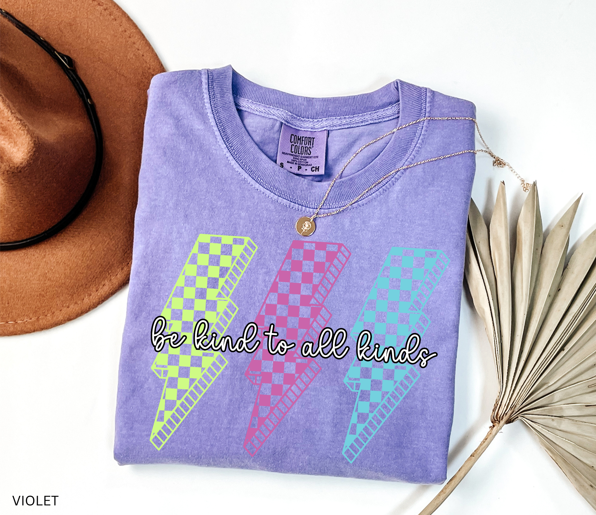Three retro lightning bolts in neon green, pink, and blue checkered patterns with the phrase “Be Kind to All Kinds.”