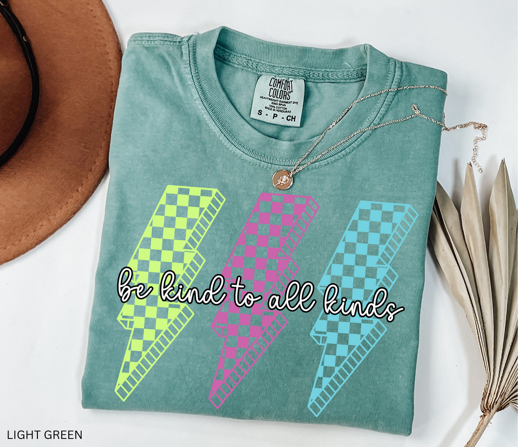 Three retro lightning bolts in neon green, pink, and blue checkered patterns with the phrase “Be Kind to All Kinds.”