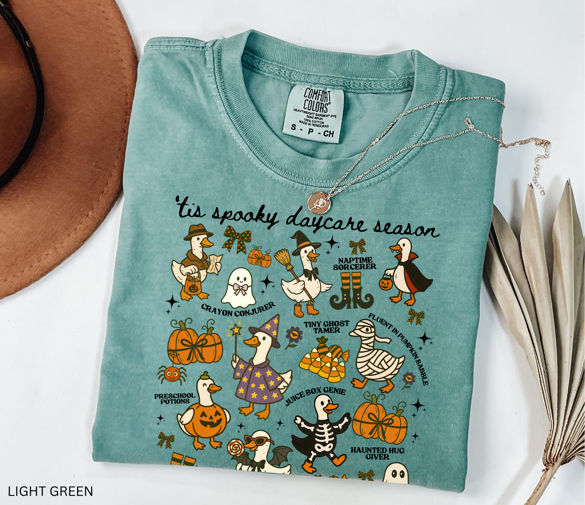 Halloween daycare teacher shirt with geese dressed in spooky costumes and playful phrases like ’Tis Spooky Daycare Season, Crayon Conjurer, and Juice Box Genie.