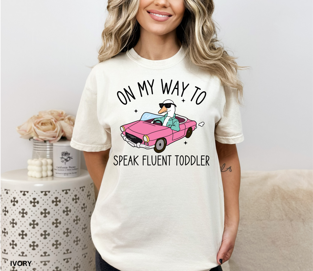 Daycare teacher shirt with a goose driving a pink convertible wearing sunglasses and the phrase ‘On My Way to Speak Fluent Toddler.