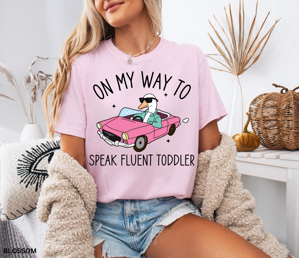 Daycare teacher shirt with a goose driving a pink convertible wearing sunglasses and the phrase ‘On My Way to Speak Fluent Toddler.