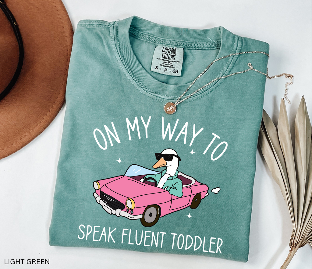 Daycare teacher shirt with a goose driving a pink convertible wearing sunglasses and the phrase ‘On My Way to Speak Fluent Toddler.