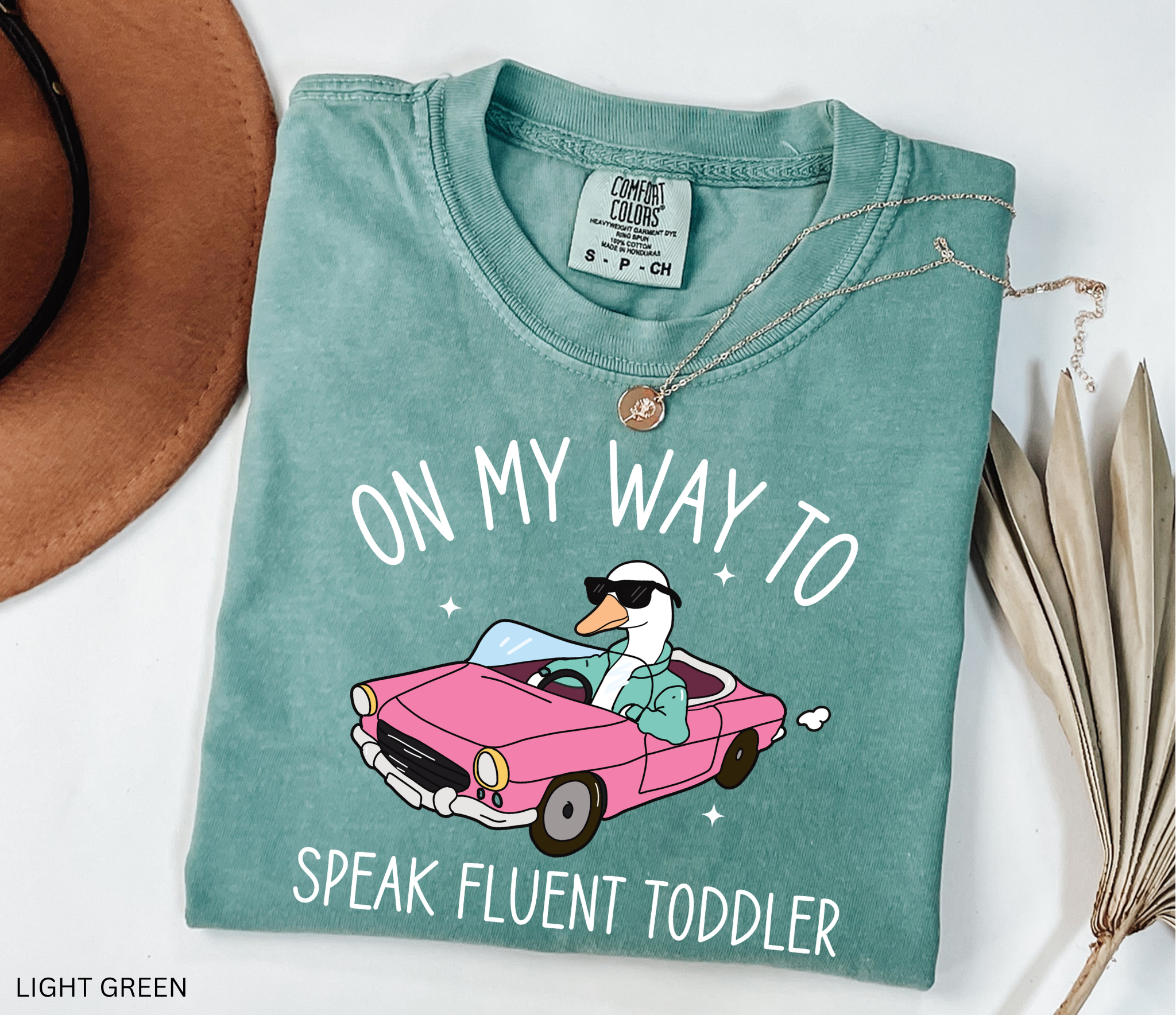 Daycare teacher shirt with a goose driving a pink convertible wearing sunglasses and the phrase ‘On My Way to Speak Fluent Toddler.