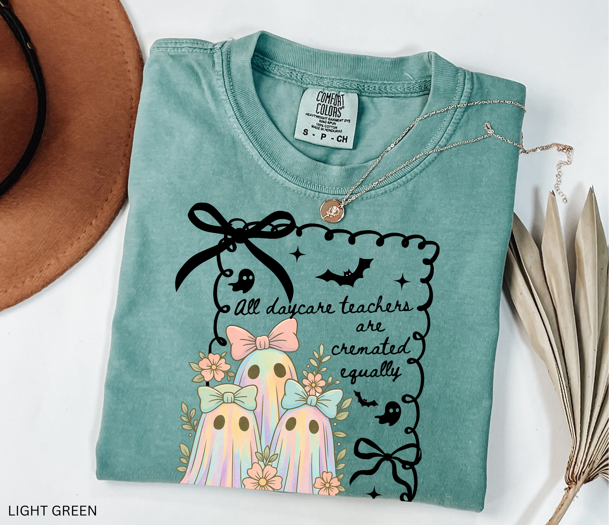 Halloween daycare teacher shirt with three pastel rainbow ghosts wearing bows, surrounded by flowers. Cute and spooky teacher tee for childcare staff.