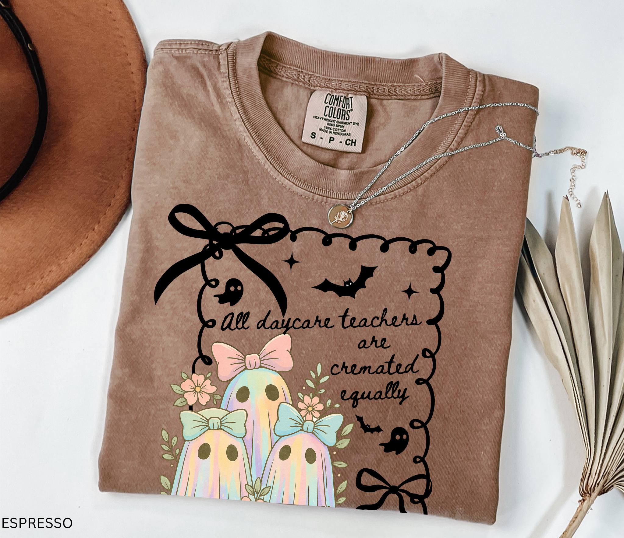 Halloween daycare teacher shirt with three pastel rainbow ghosts wearing bows, surrounded by flowers. Cute and spooky teacher tee for childcare staff.
