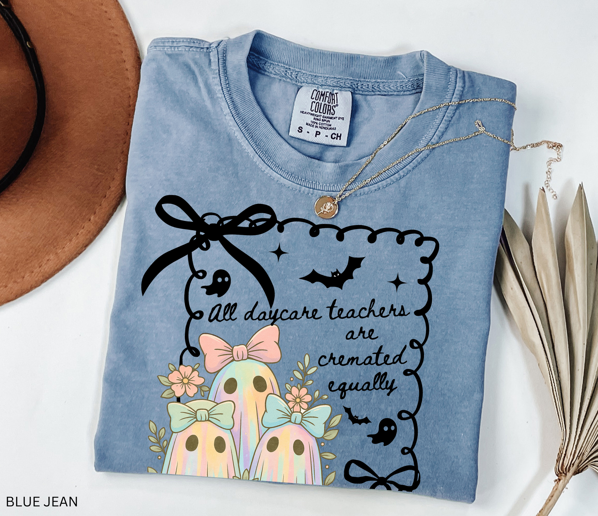 Halloween daycare teacher shirt with three pastel rainbow ghosts wearing bows, surrounded by flowers. Cute and spooky teacher tee for childcare staff.