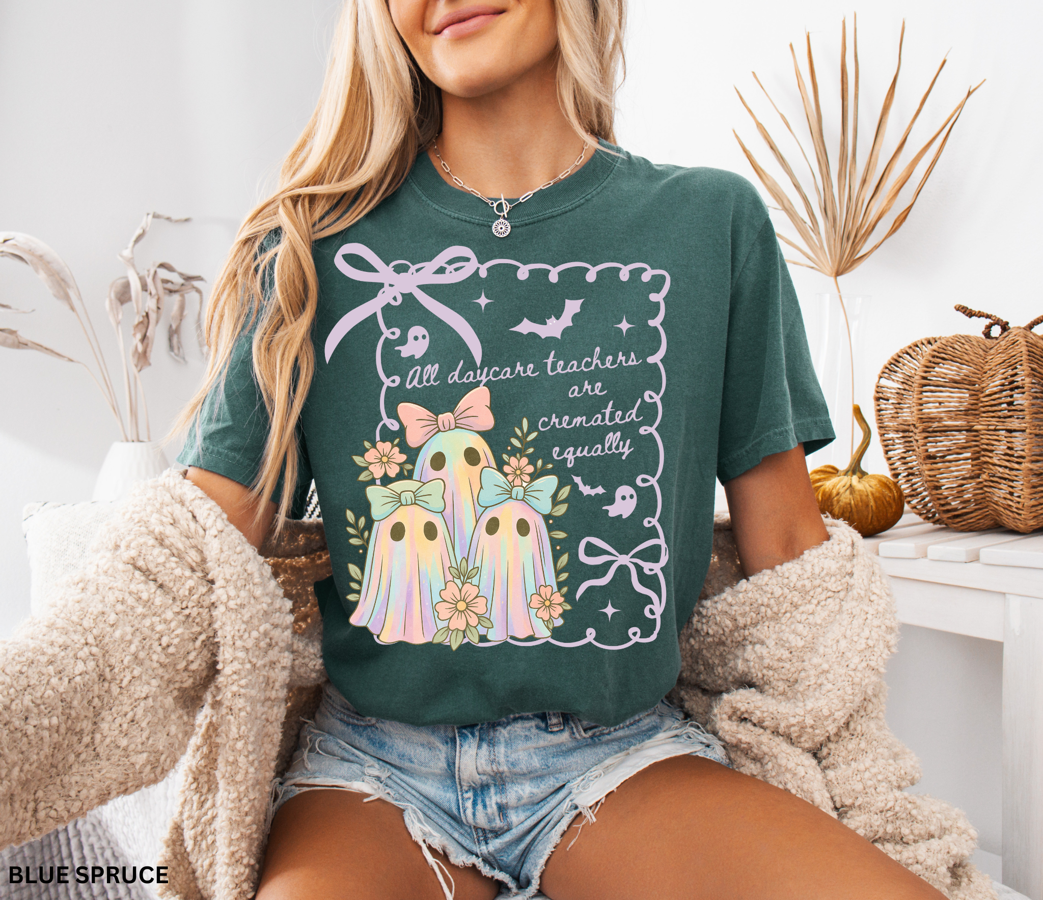 Halloween daycare teacher shirt with three pastel rainbow ghosts wearing bows, surrounded by flowers. Cute and spooky teacher tee for childcare staff.