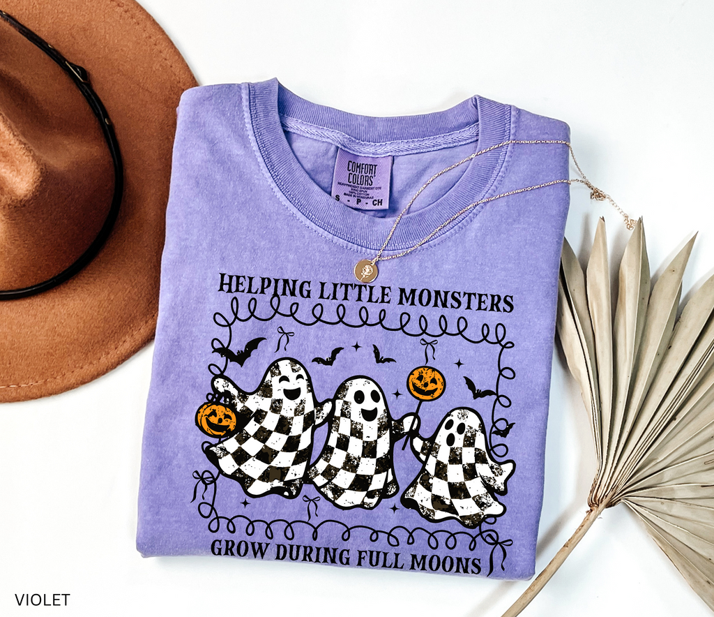 Halloween daycare teacher shirt with three checkered black-and-white ghosts holding pumpkins and lollipops, surrounded by bats. Cute spooky tee