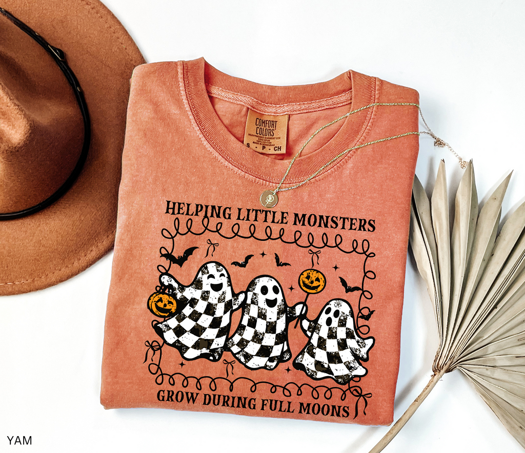 Halloween daycare teacher shirt with three checkered black-and-white ghosts holding pumpkins and lollipops, surrounded by bats. Cute spooky tee
