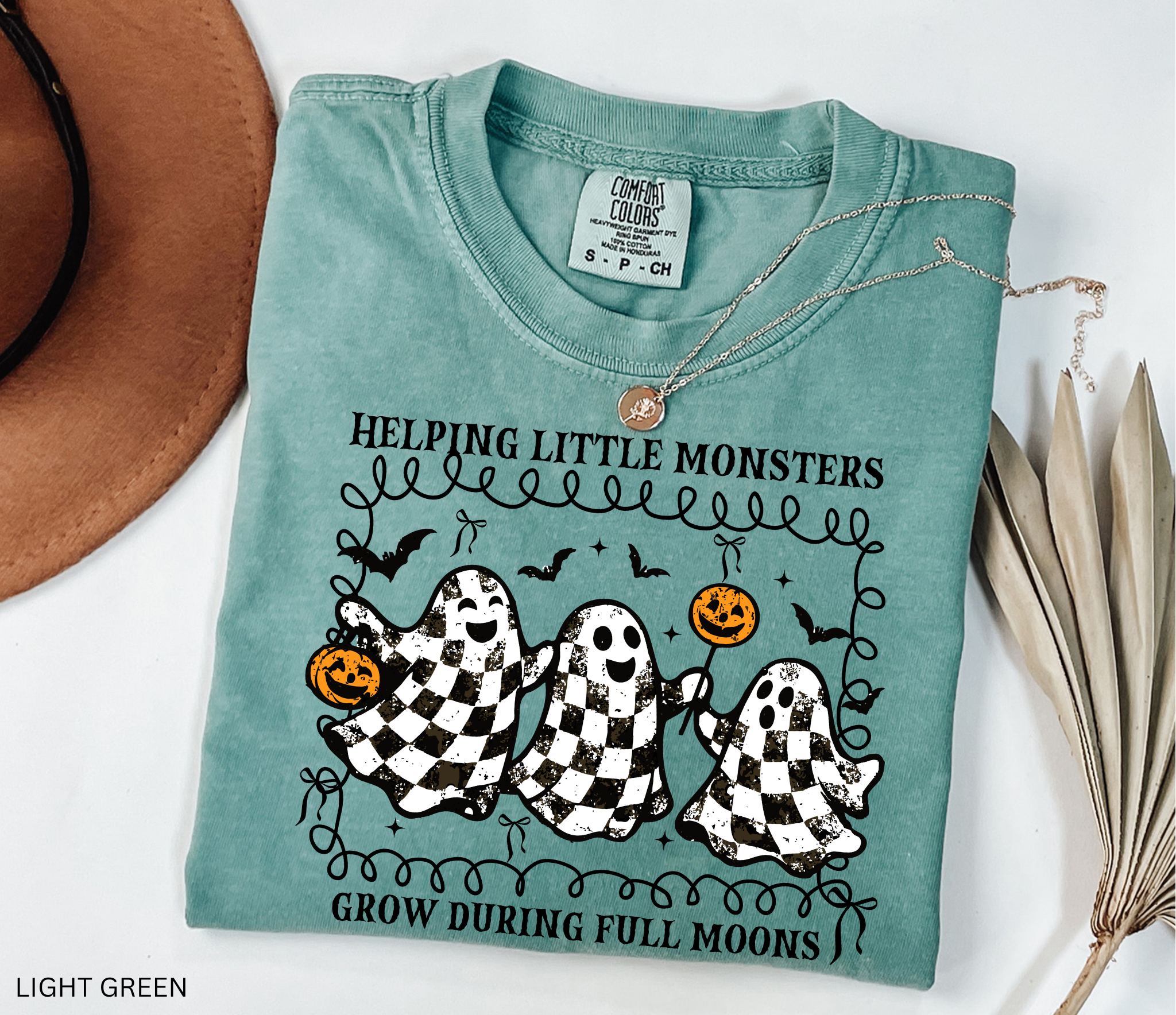 Halloween daycare teacher shirt with three checkered black-and-white ghosts holding pumpkins and lollipops, surrounded by bats. Cute spooky tee