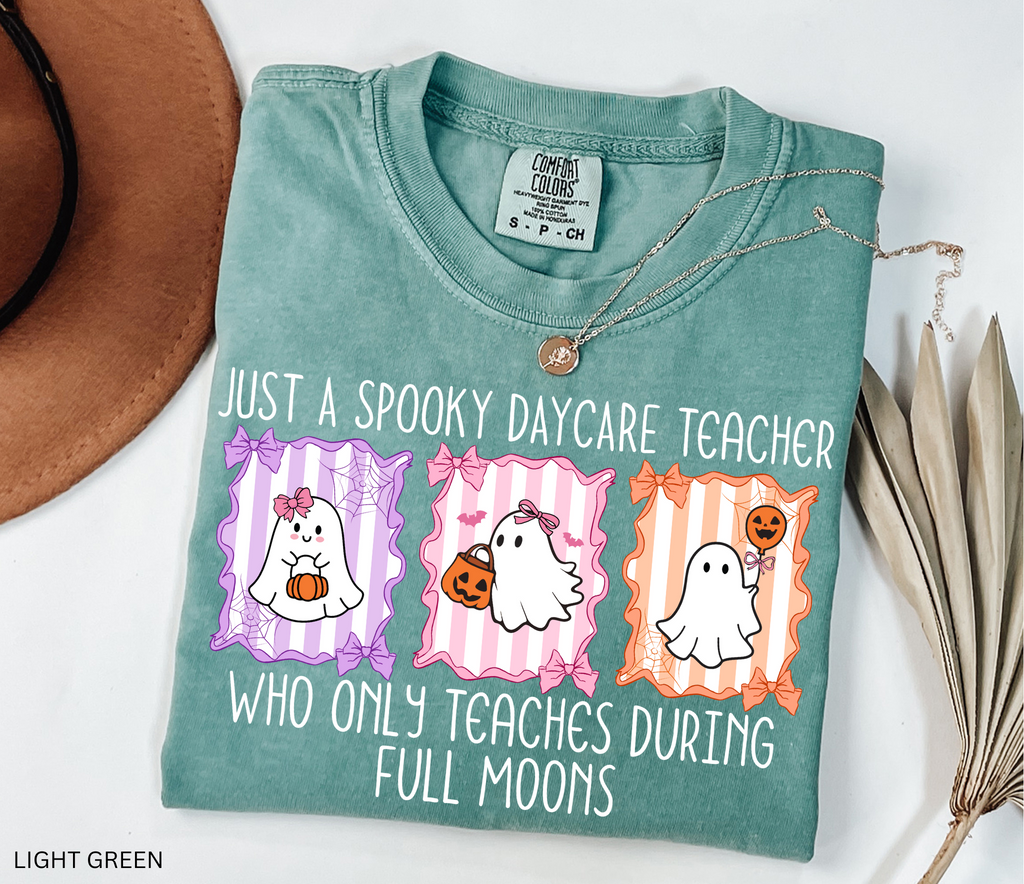 Halloween daycare teacher shirt with three pastel ghosts holding pumpkins, framed with bows and spiderwebs. Text says Just a spooky daycare teacher who only teaches during full moons.