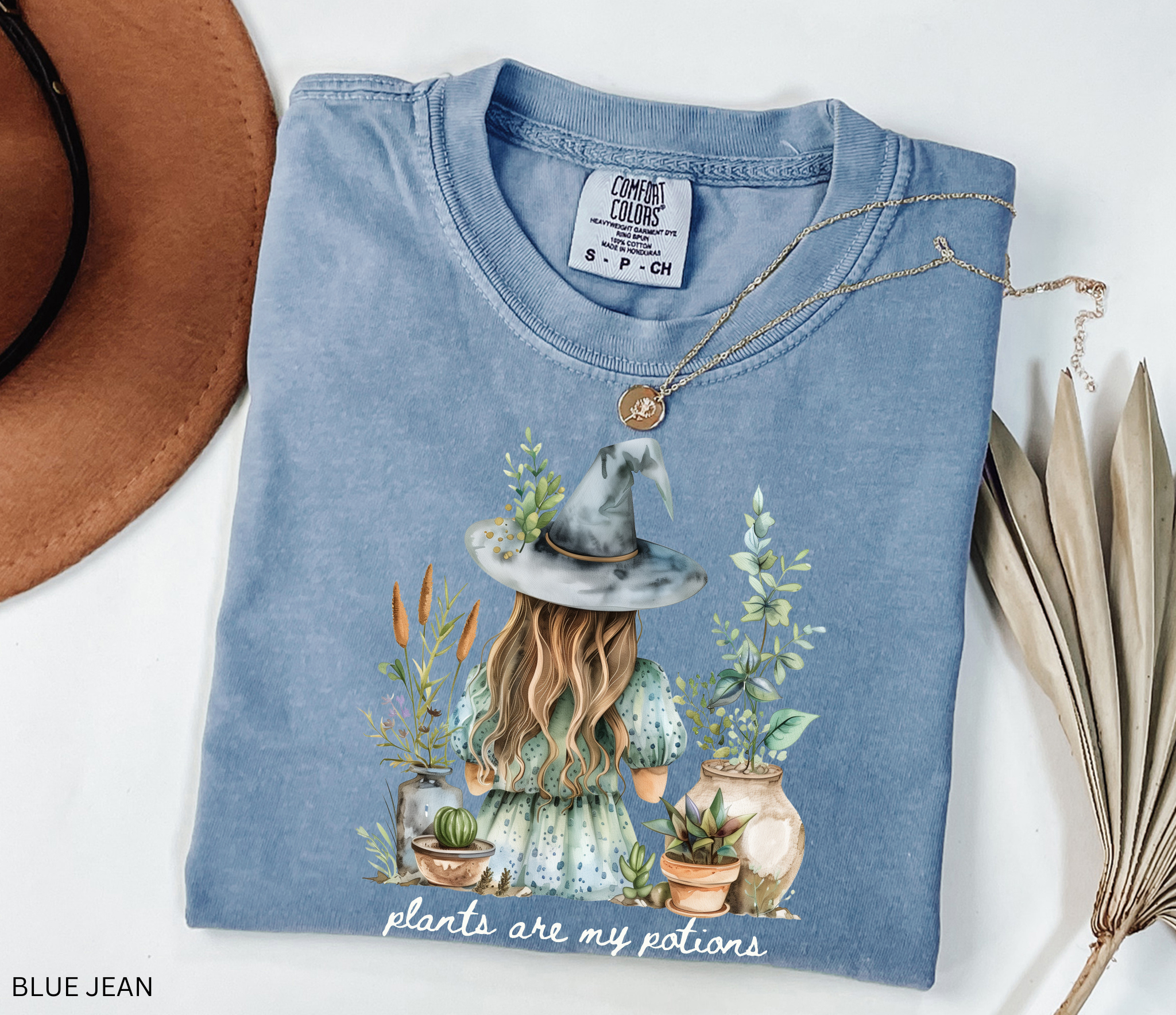Witchy plant lover t-shirt with illustration of a witch in a hat surrounded by herbs and potted plants. Cottagecore gardening and green witch aesthetic.