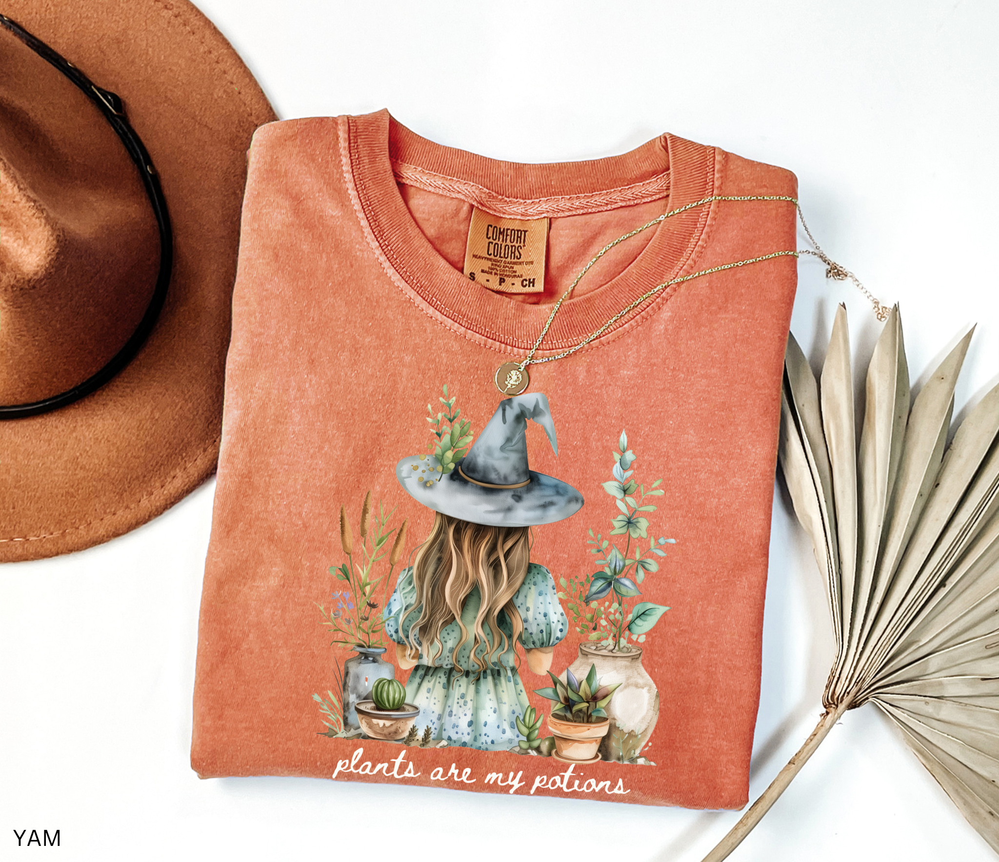 Witchy plant lover t-shirt with illustration of a witch in a hat surrounded by herbs and potted plants. Cottagecore gardening and green witch aesthetic.