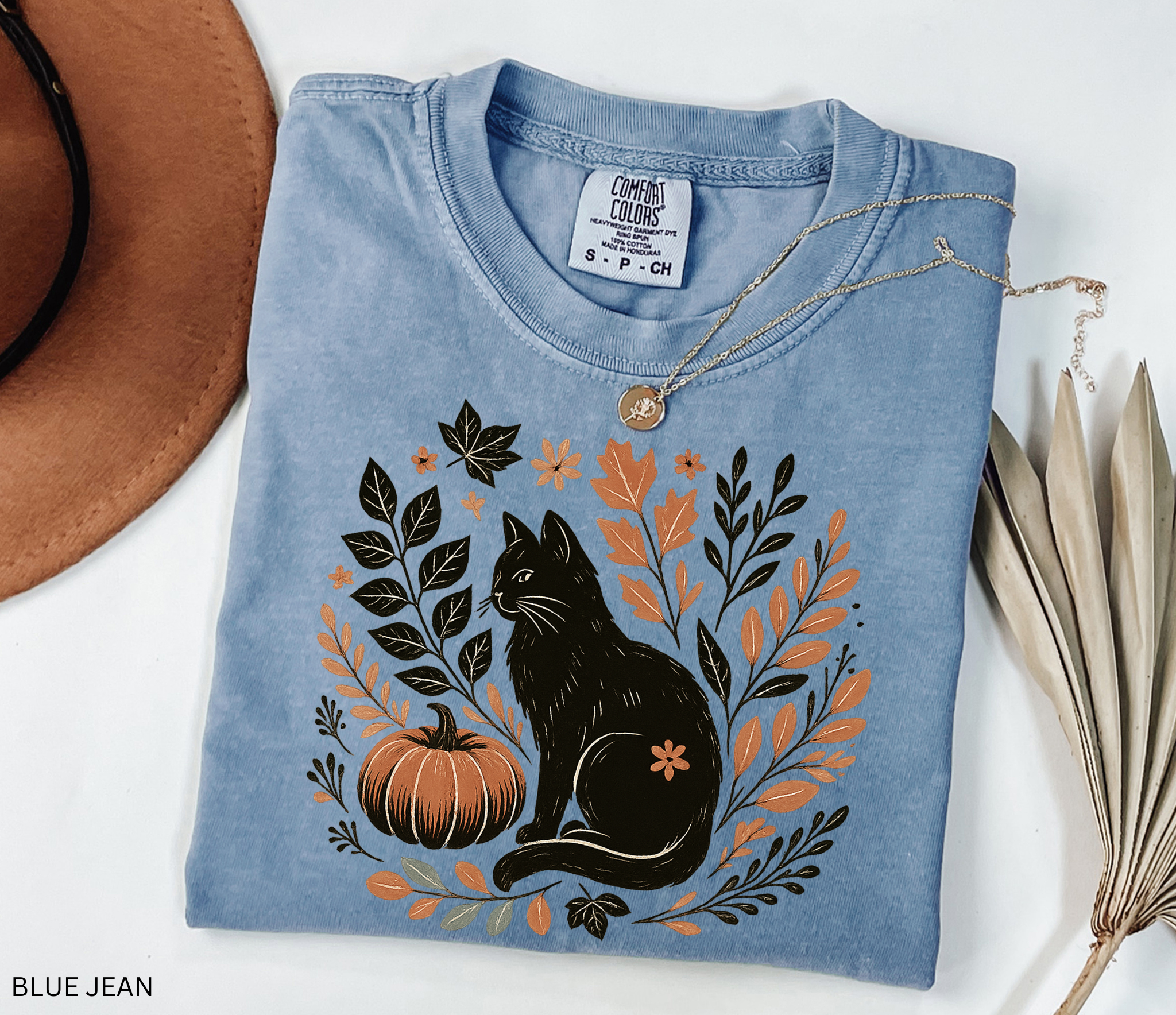 “Halloween cottagecore shirt with a vintage black cat sitting beside a pumpkin surrounded by autumn leaves and florals in a hand-drawn style.