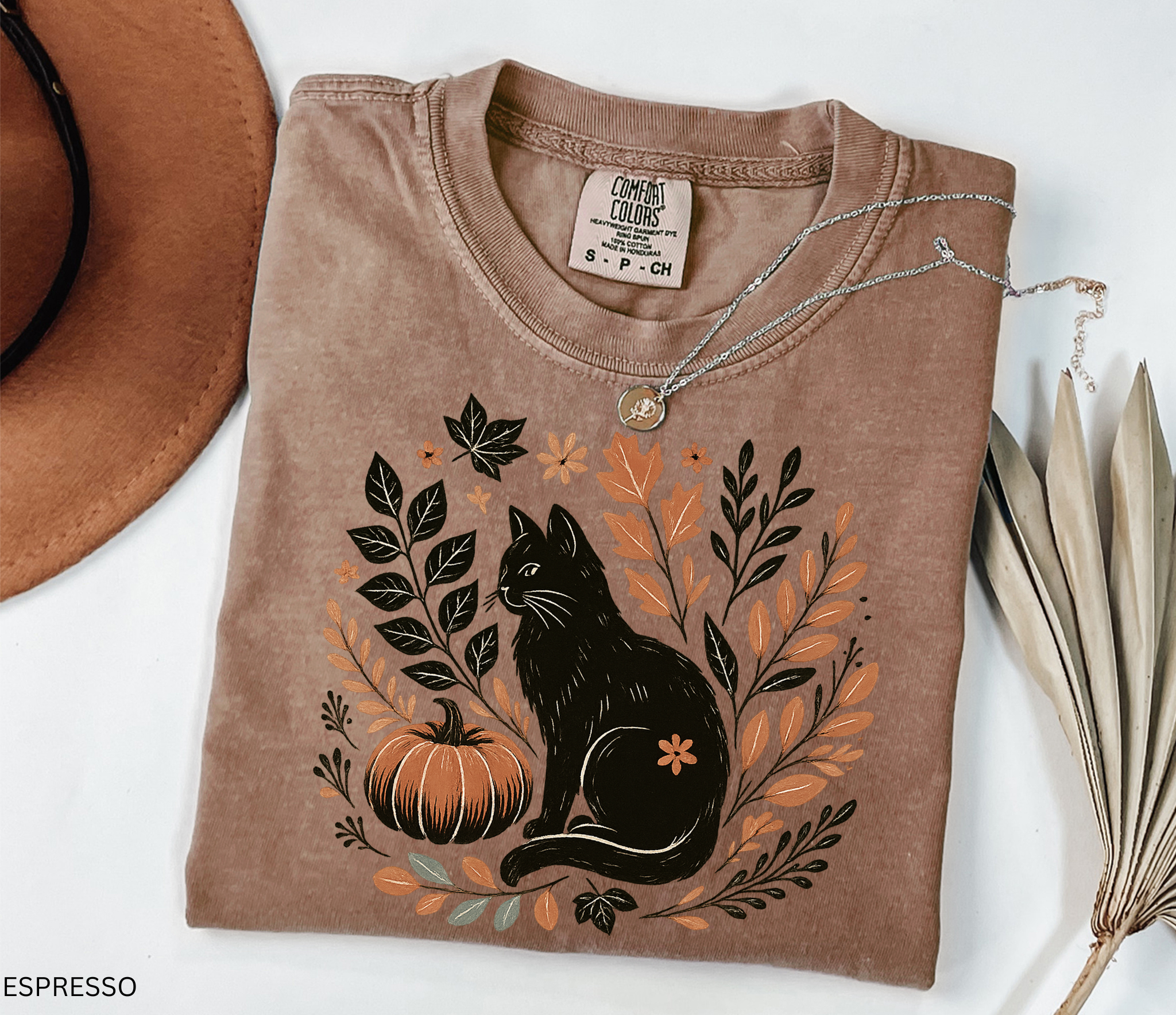 “Halloween cottagecore shirt with a vintage black cat sitting beside a pumpkin surrounded by autumn leaves and florals in a hand-drawn style.