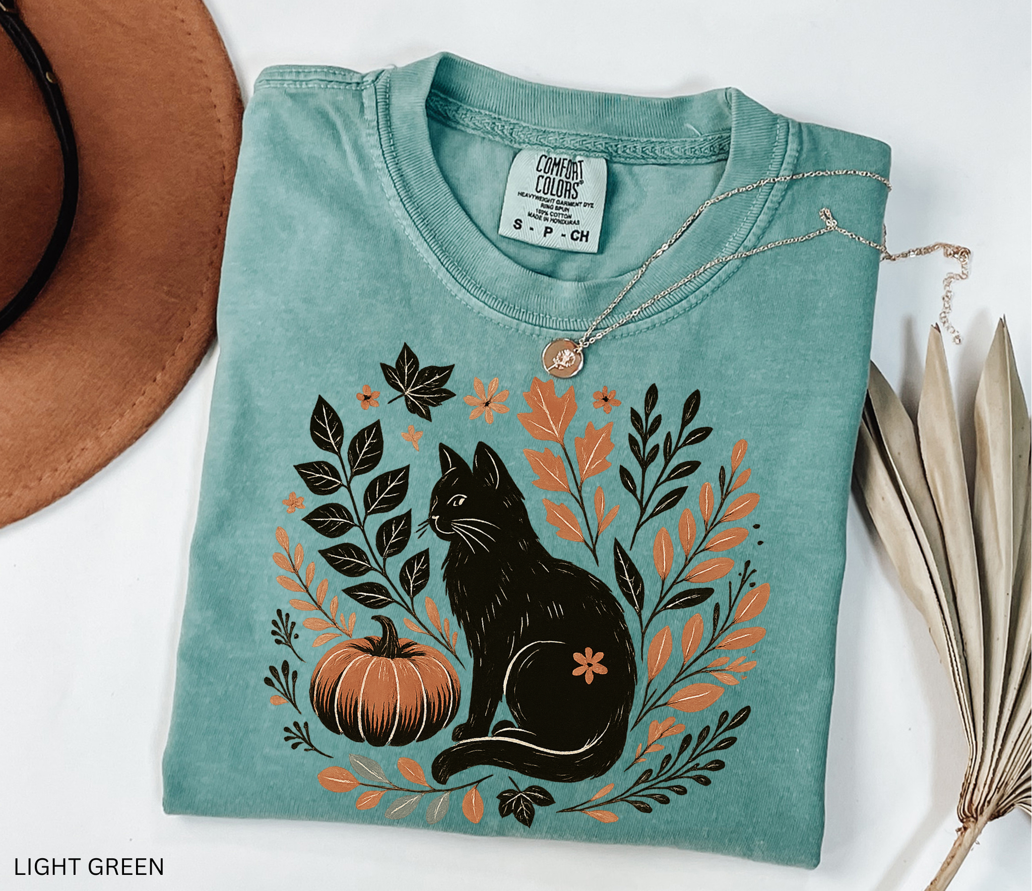 “Halloween cottagecore shirt with a vintage black cat sitting beside a pumpkin surrounded by autumn leaves and florals in a hand-drawn style.