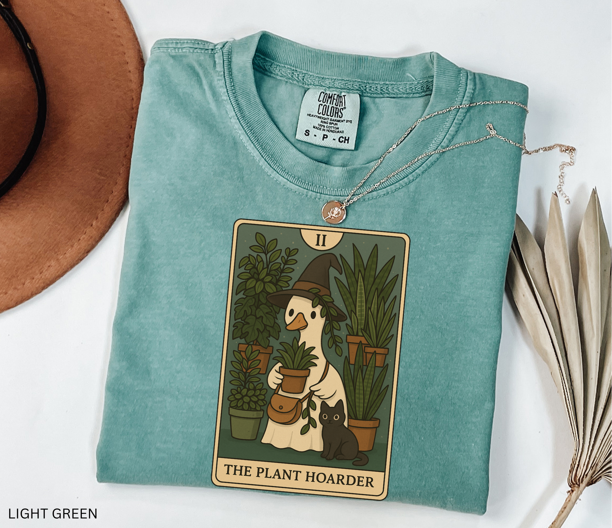 Witchy plant hoarder shirt featuring a tarot card design of a goose in a witch hat holding plants, surrounded by greenery and a black cat.