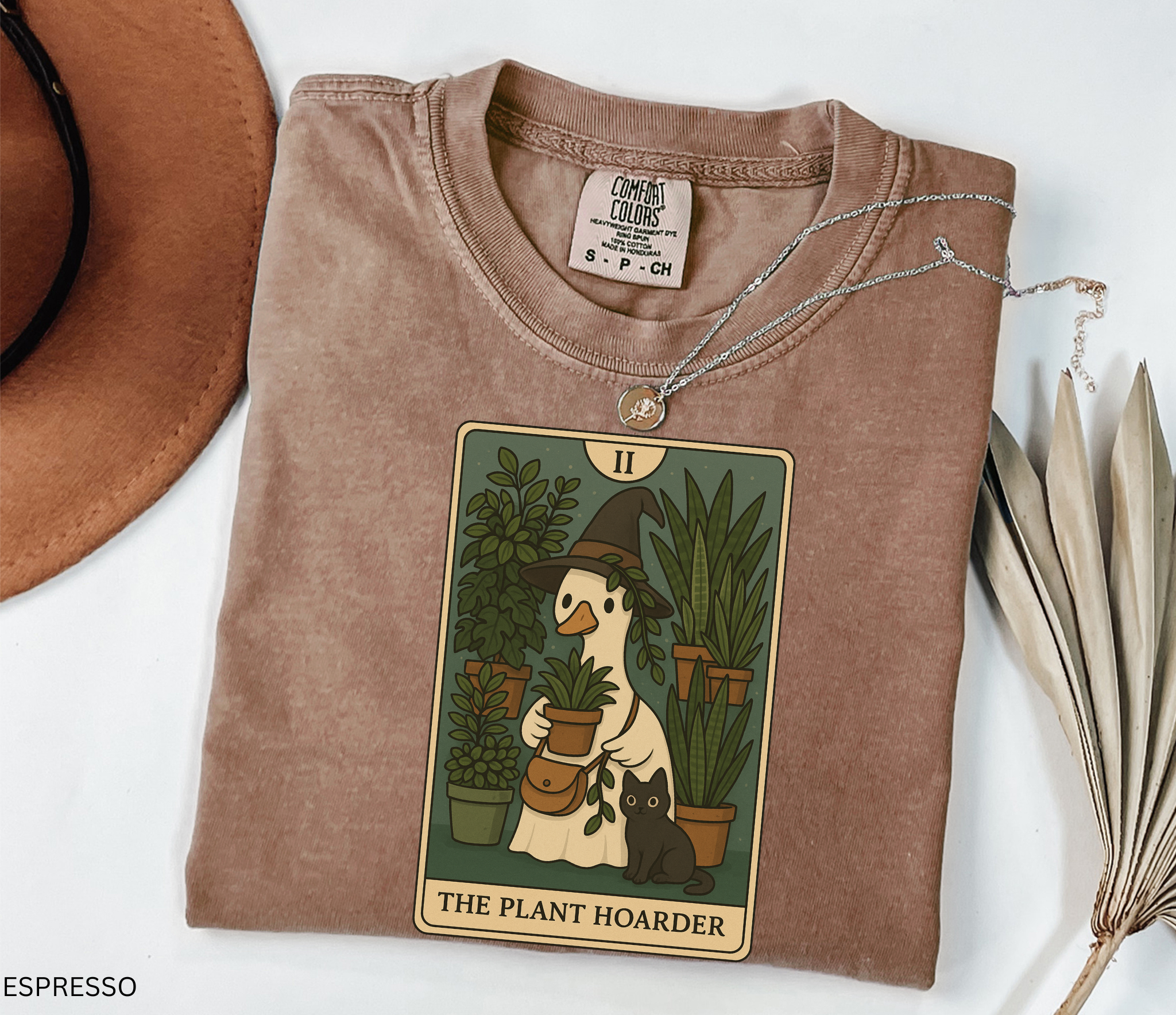 Witchy plant hoarder shirt featuring a tarot card design of a goose in a witch hat holding plants, surrounded by greenery and a black cat.