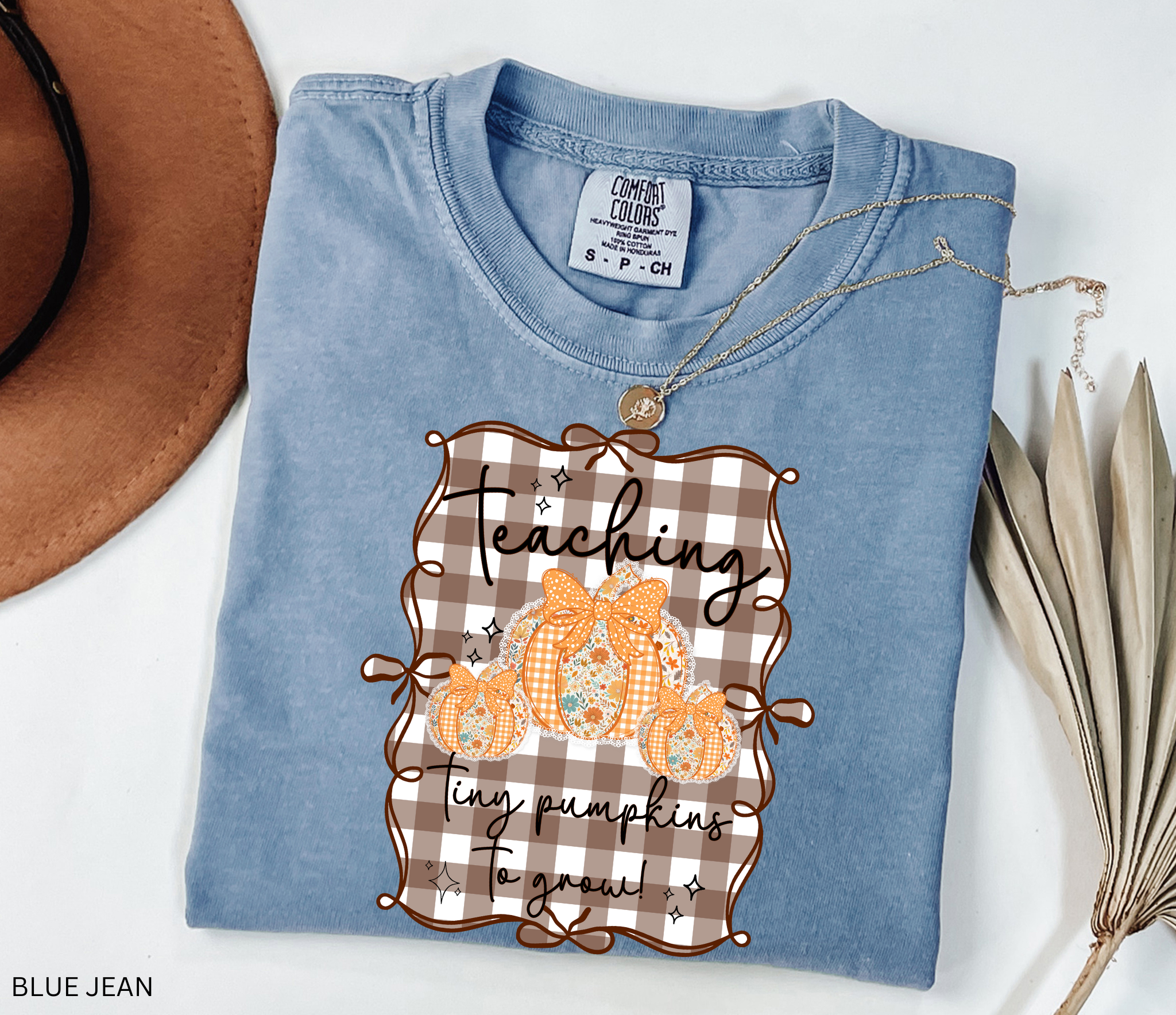 Brown gingham background Halloween teacher shirt with three floral orange pumpkins tied in bows and the phrase “Teaching Tiny Pumpkins to Grow.”
