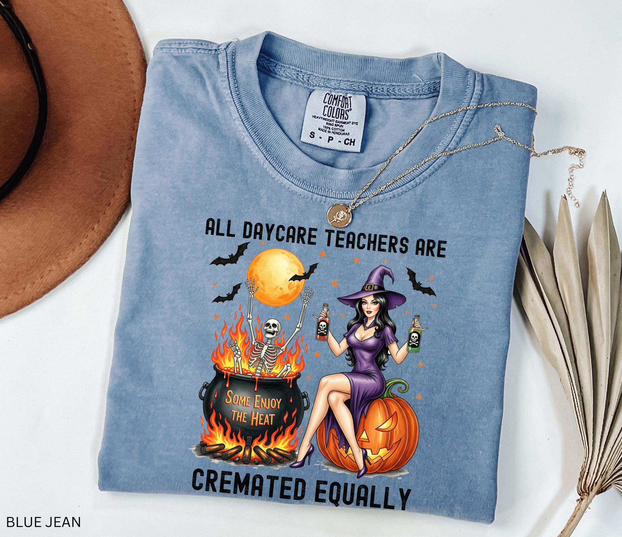 Halloween shirt design featuring a witch in a purple dress sitting on a pumpkin, holding potion bottles, with a skeleton in a fiery cauldron under a full moon.
