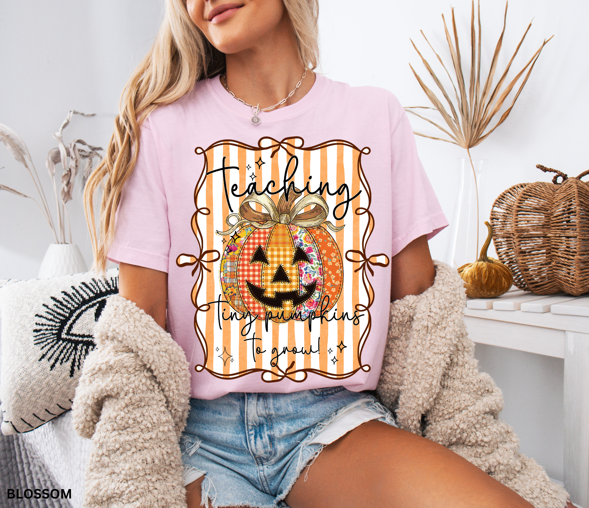 Halloween teacher shirt with an orange patchwork jack-o’-lantern tied in a bow on a striped background and the phrase “Teaching Tiny Pumpkins to Grow.”